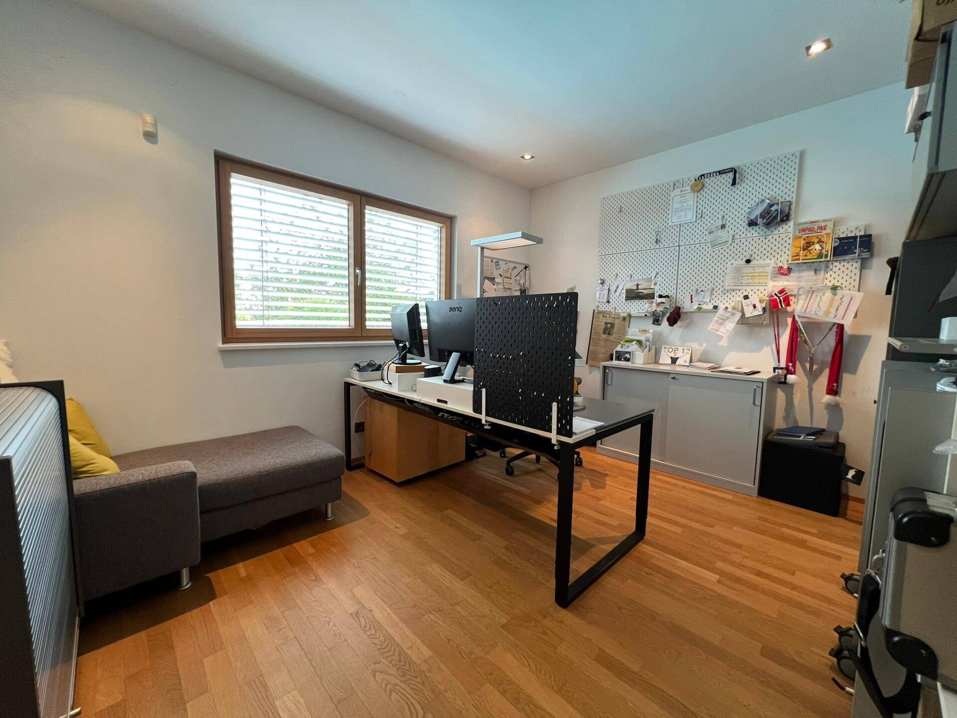 Helles Büro mit Holzparkett, einem großen Schreibtisch und zwei Monitoren, ideal für konzentriertes Arbeiten.