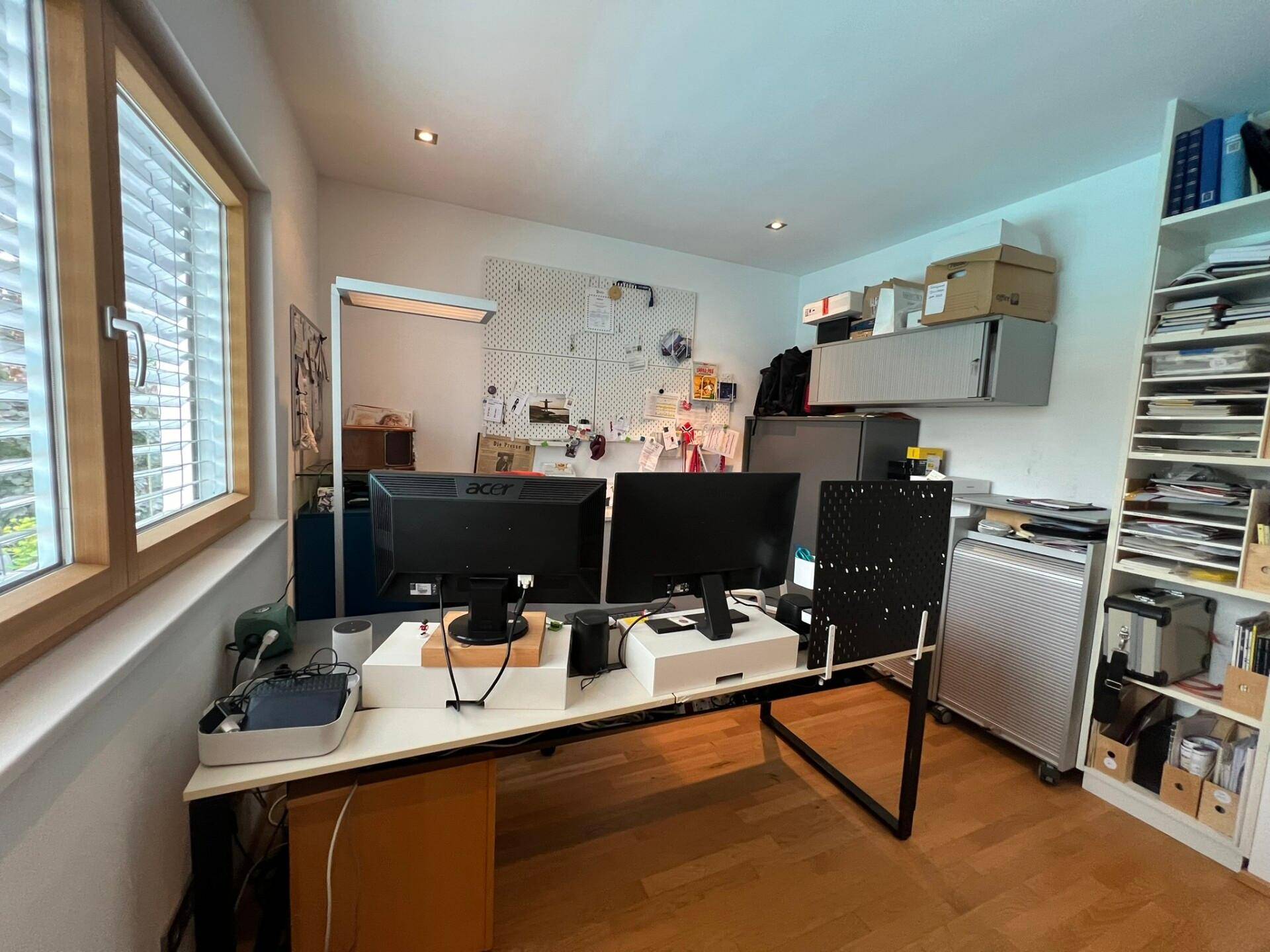 Gut beleuchtetes Büro mit Holzparkett, einem organisierten Schreibtischbereich und praktischen Regalen.