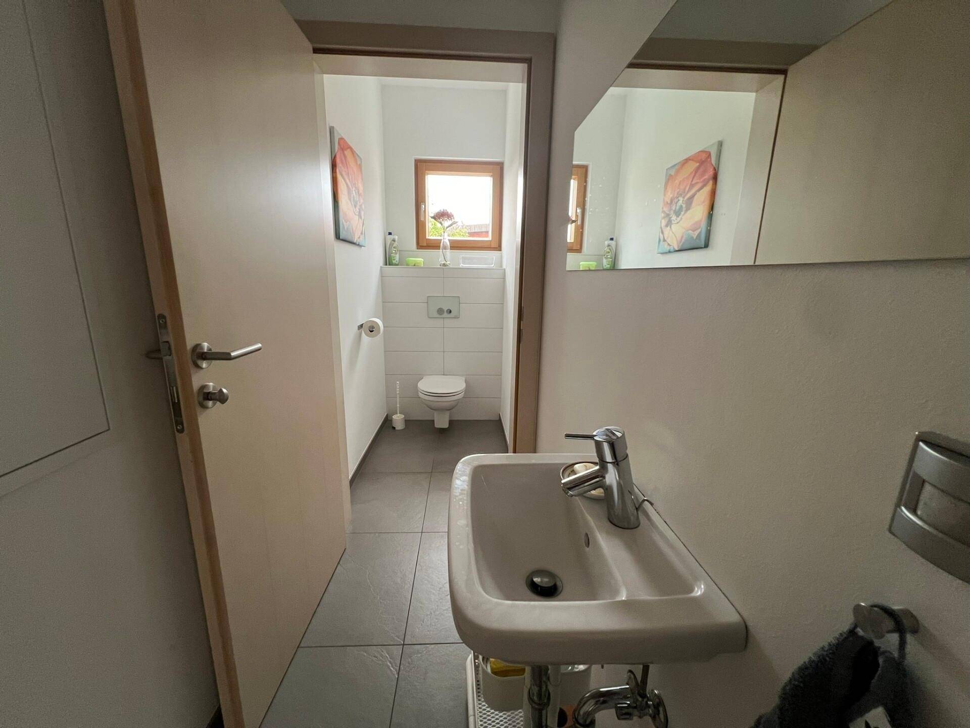 Modernes Gäste-WC mit Fliesenboden, einem Waschbecken und einem Fenster für natürliche Belüftung.