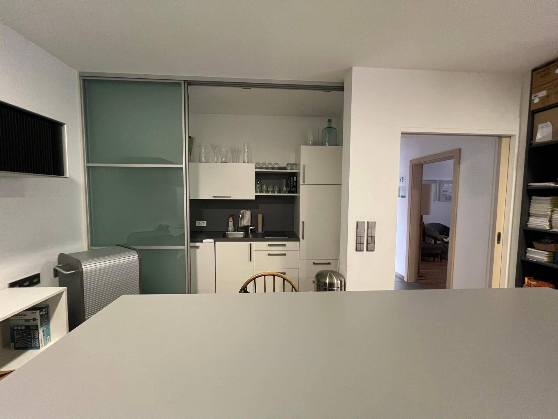 Kompakte Teeküche mit weißen Schränken und integrierten Geräten, ideal für schnelle Pausen im Büro.