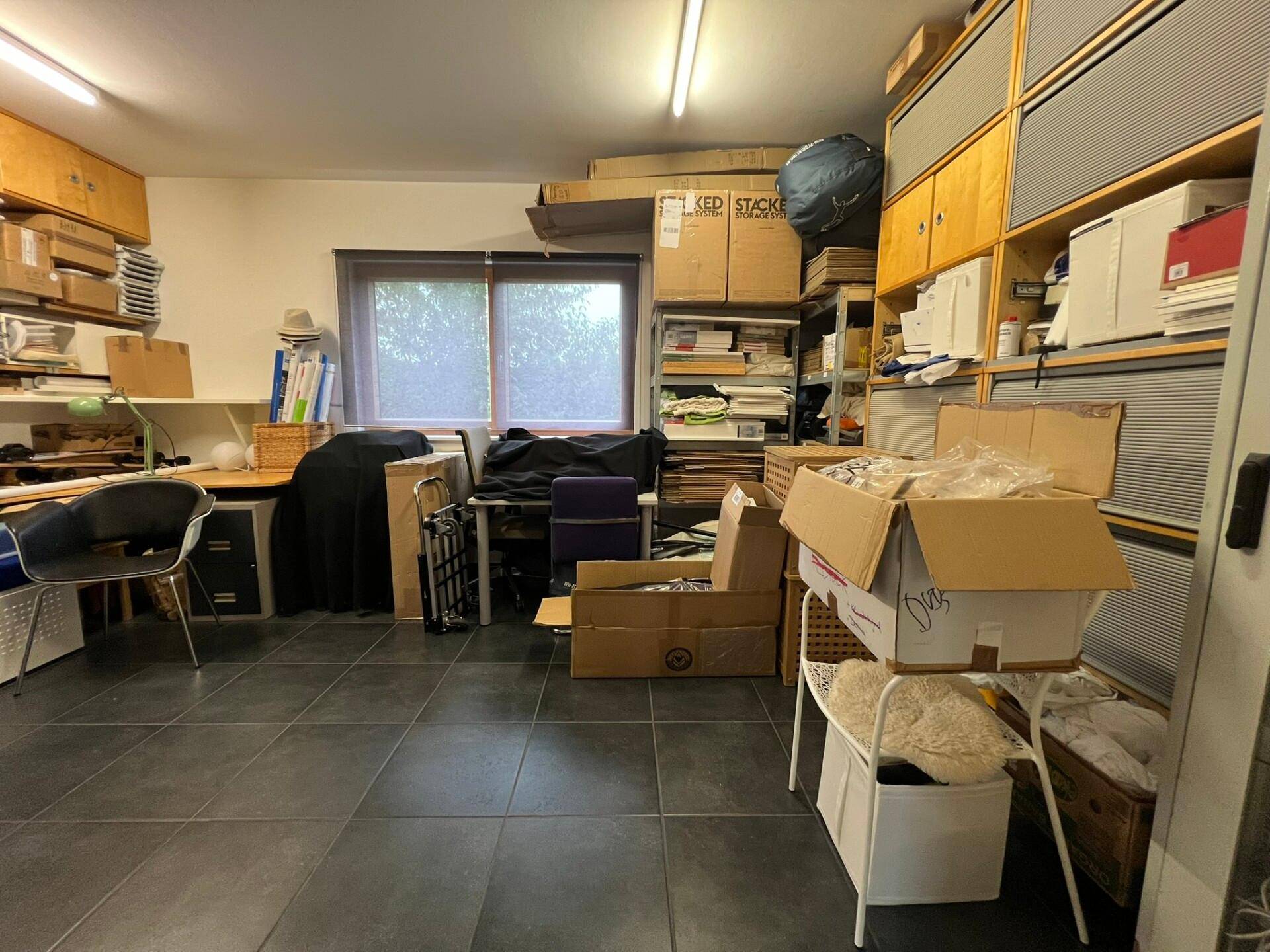 Geräumiger Lagerraum mit Fliesenboden und zahlreichen Regalen, gefüllt mit Kartons und Büromaterial.