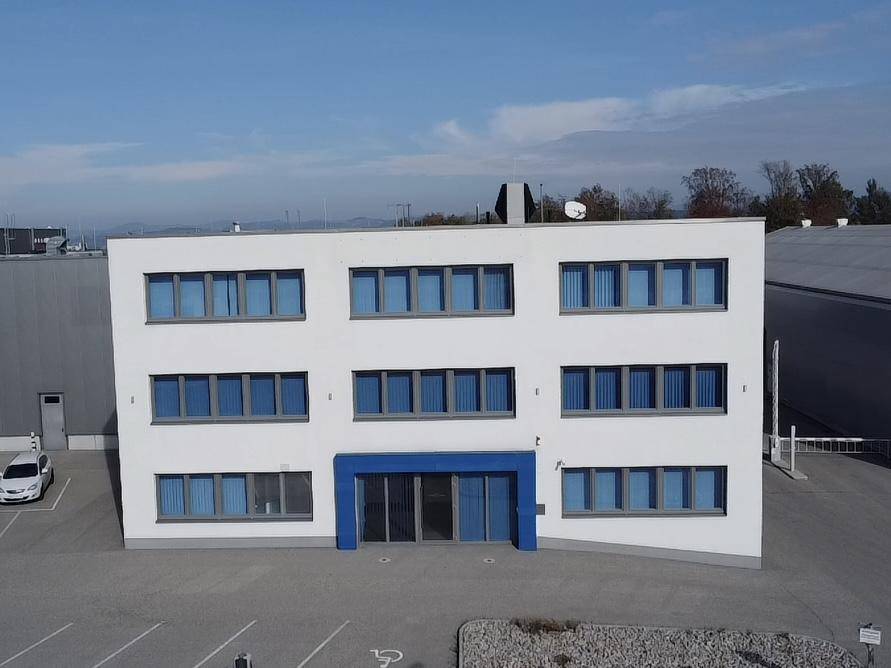 Frontansicht des modernen Bürogebäudes mit weißer Fassade, blauen Fenstern und Parkplätzen unter blauem Himmel.