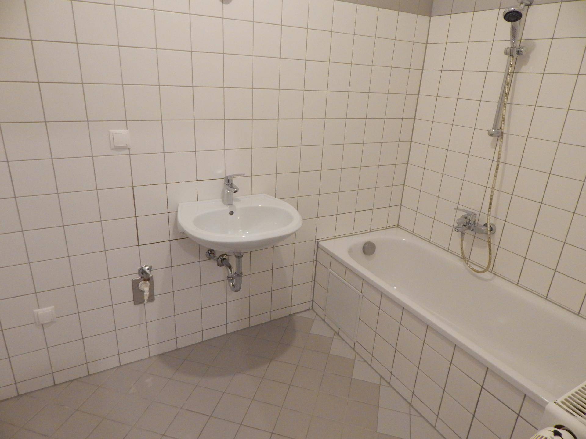 Badezimmer mit weißen Fliesen, Badewanne und Waschbecken.