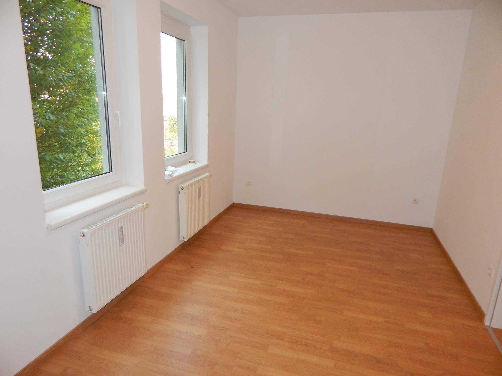 Helles Schlafzimmer mit Laminatboden und zwei Fenstern mit Blick ins Grüne.