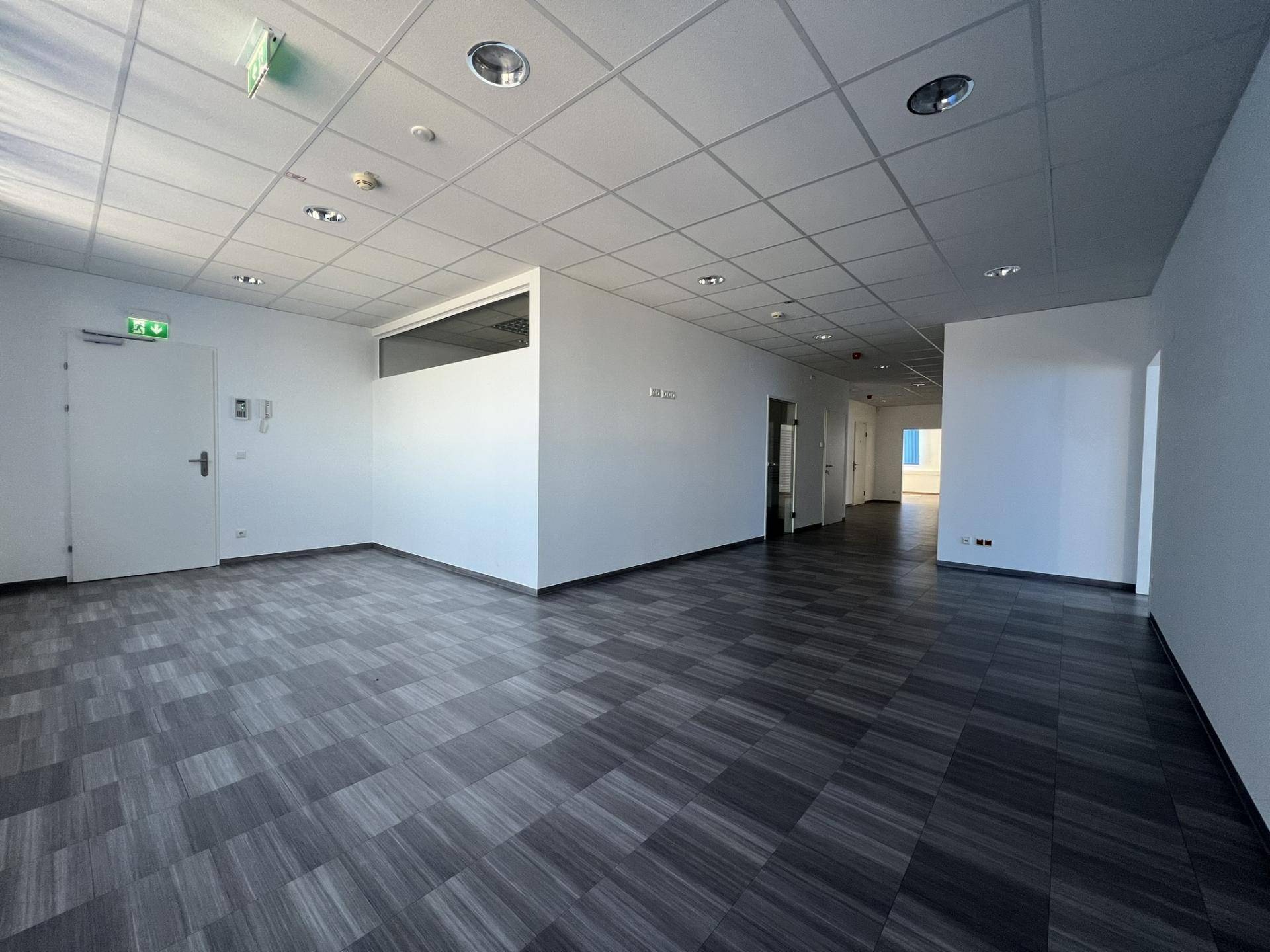 Geräumiger, leerer Büroraum mit Teppichfliesen, weißen Wänden und abgehängter Decke, bereit zur Nutzung.