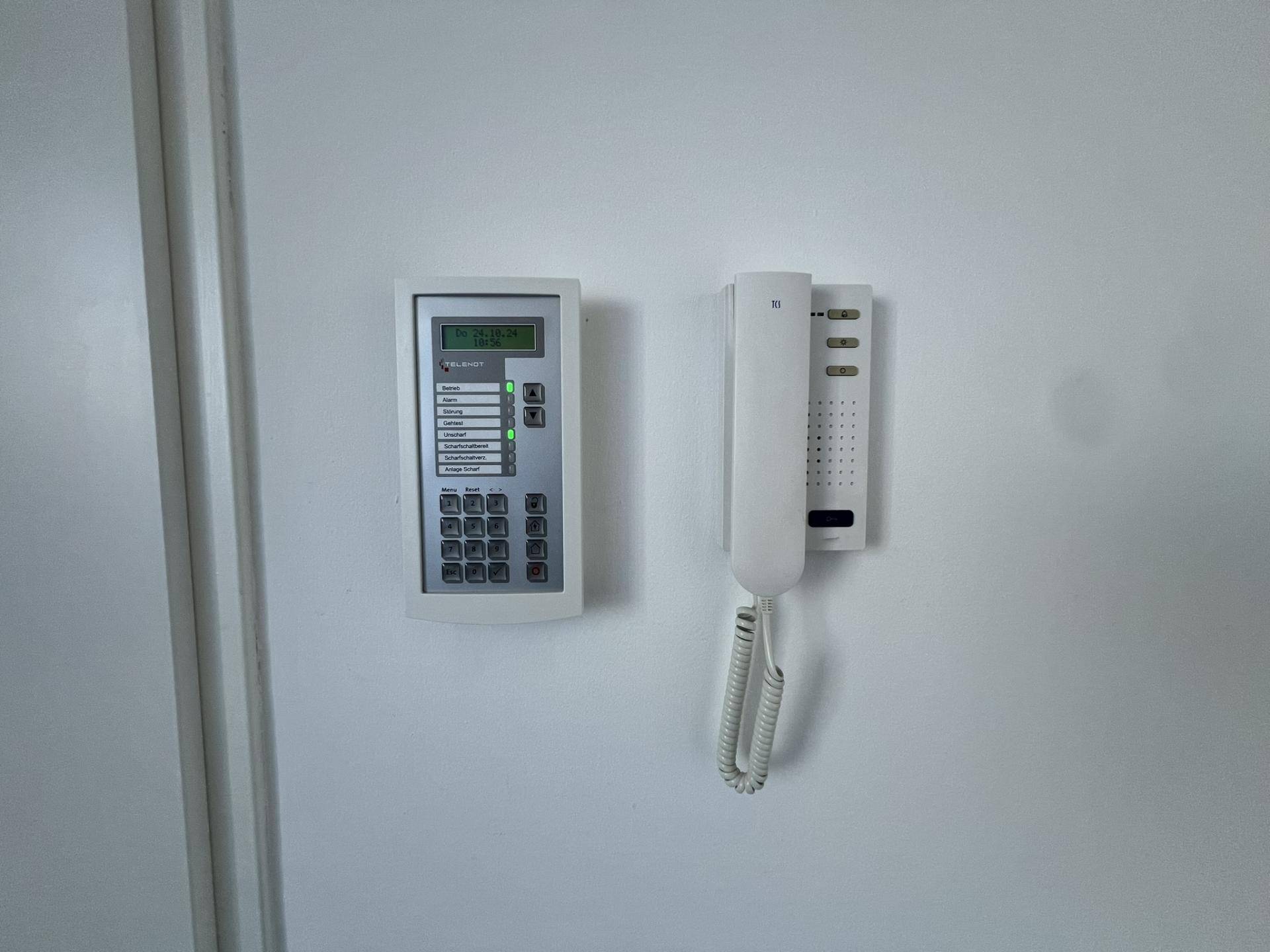 Detailansicht einer modernen Gegensprechanlage und eines Telefons an einer weißen Wand im Eingangsbereich.