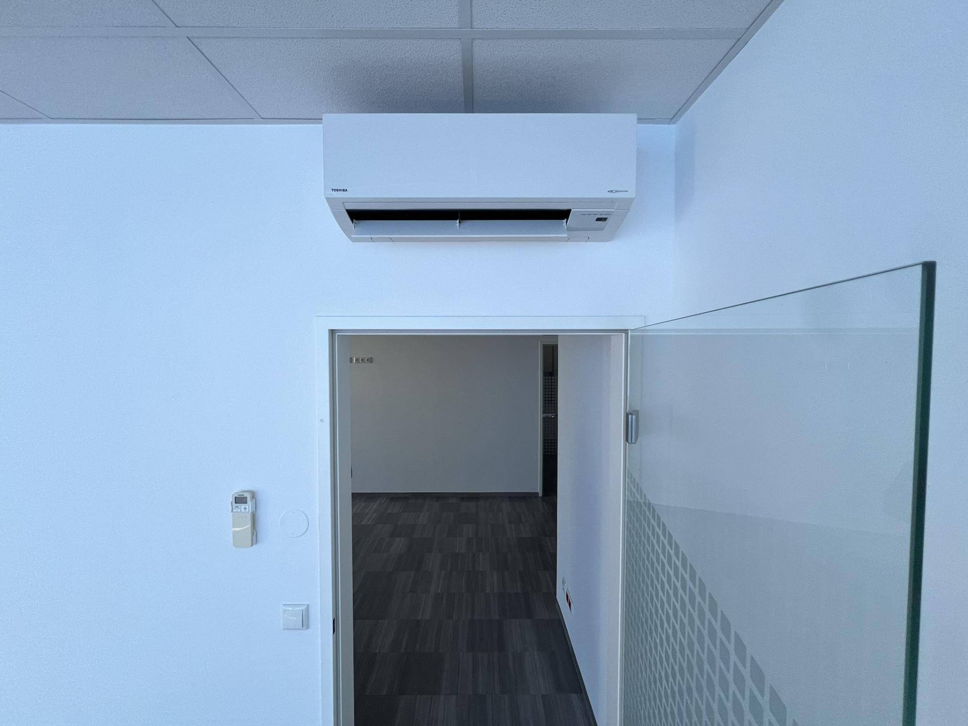 Büroraum mit Klimaanlage über der Tür und Blick auf den dunklen Boden und die weißen Wände, modern ausgestattet.