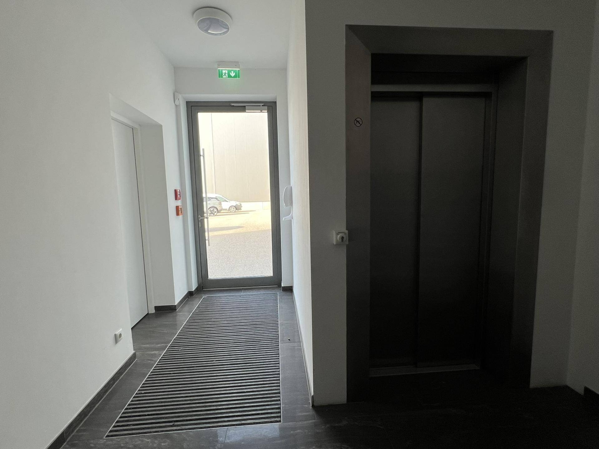 Eingangsbereich mit Aufzug, Glastür und Fußmatte, der zu den Büroräumen führt, hell und funktional.