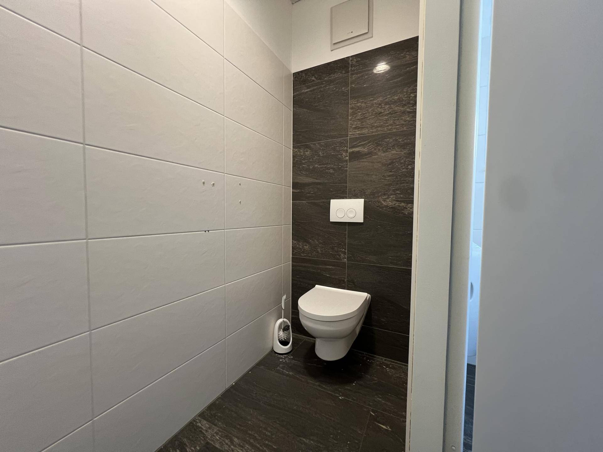 Saubere Toilette mit wandhängendem WC, dunklen und hellen Fliesen sowie einem Abluftventilator, modern gestaltet.