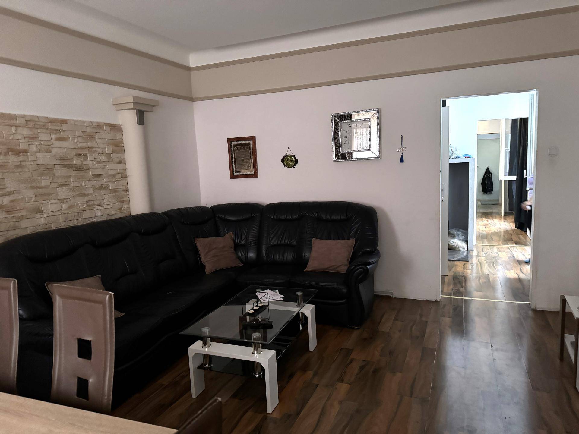 Gemütliches Wohnzimmer mit dunklem Ledersofa, Holzboden und einer strukturierten Wandverkleidung.