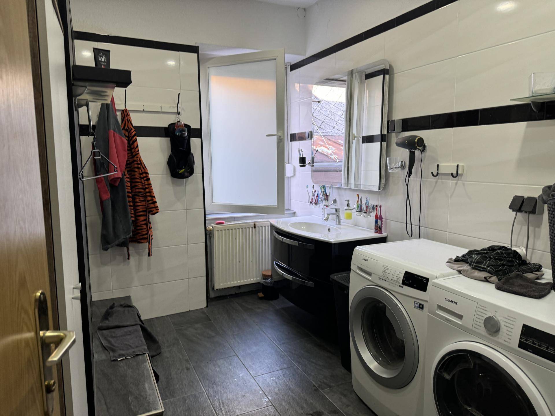 Modernes Badezimmer mit Waschmaschine, Trockner und einem Fenster für natürliche Belüftung.