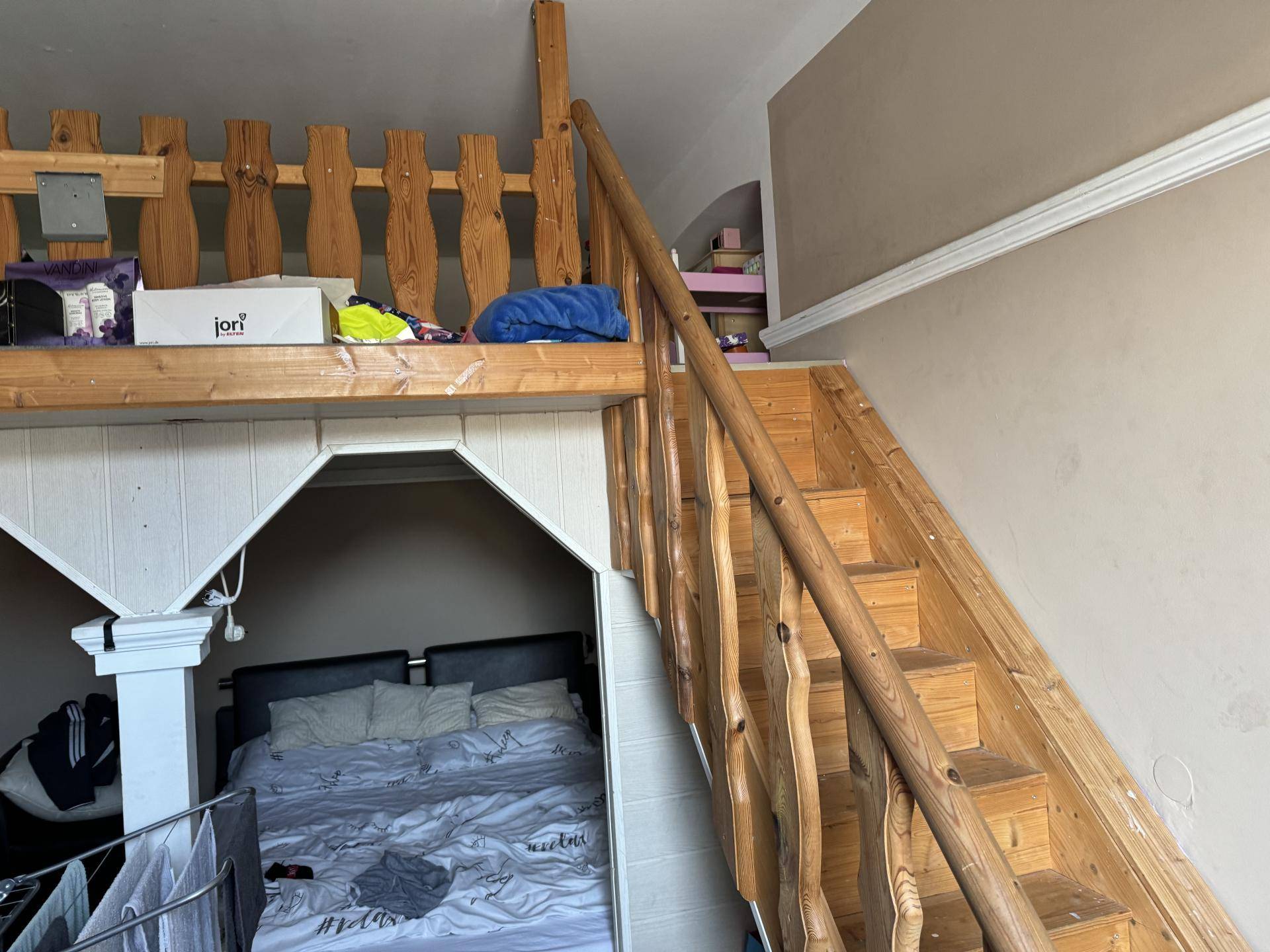 Schlafbereich unter einer Holzgalerie mit einer Treppe, die zum oberen Bereich führt.