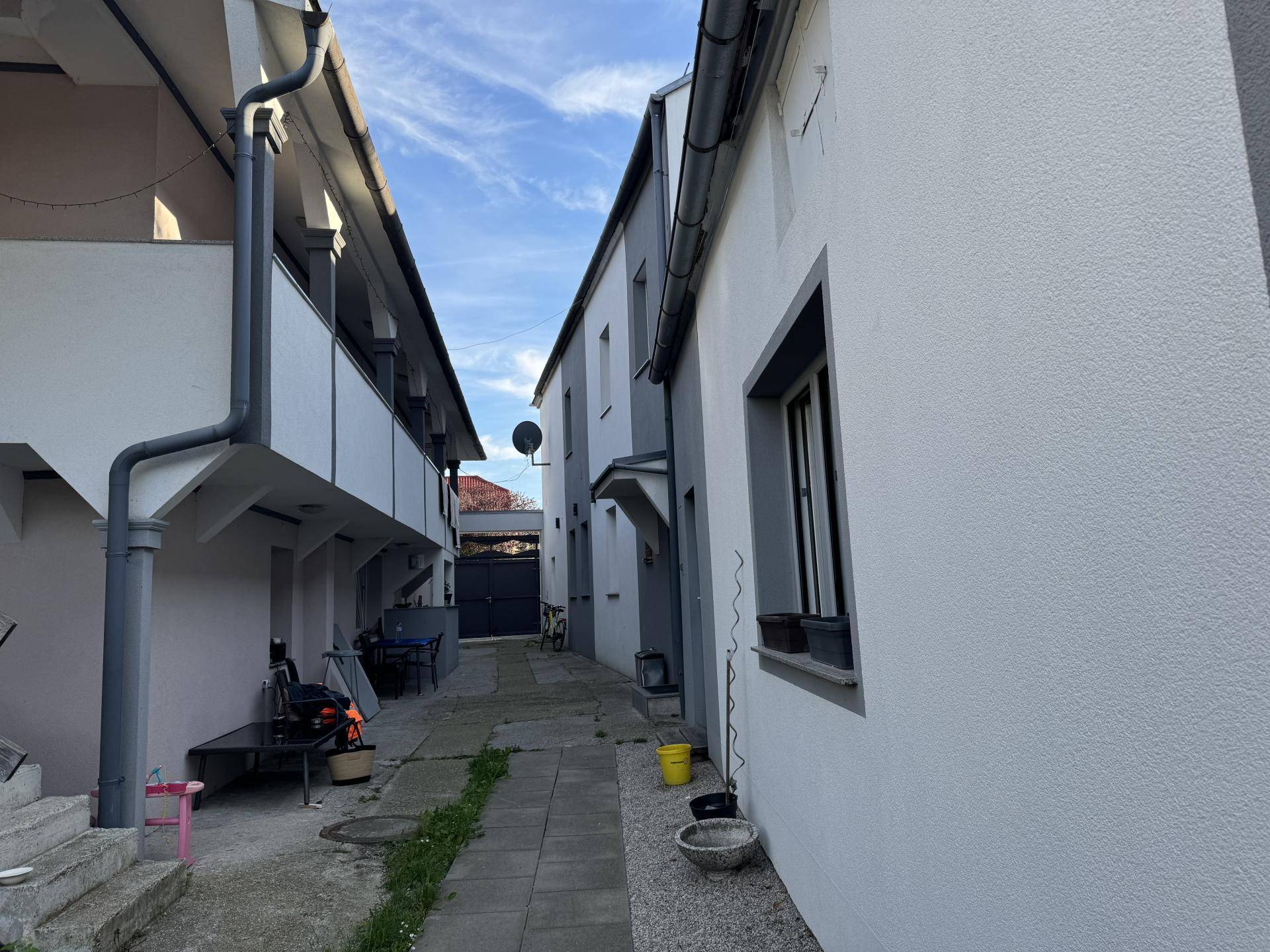 Schmaler Durchgang zwischen zwei Gebäuden mit Balkonen und einem Garagentor im Hintergrund.