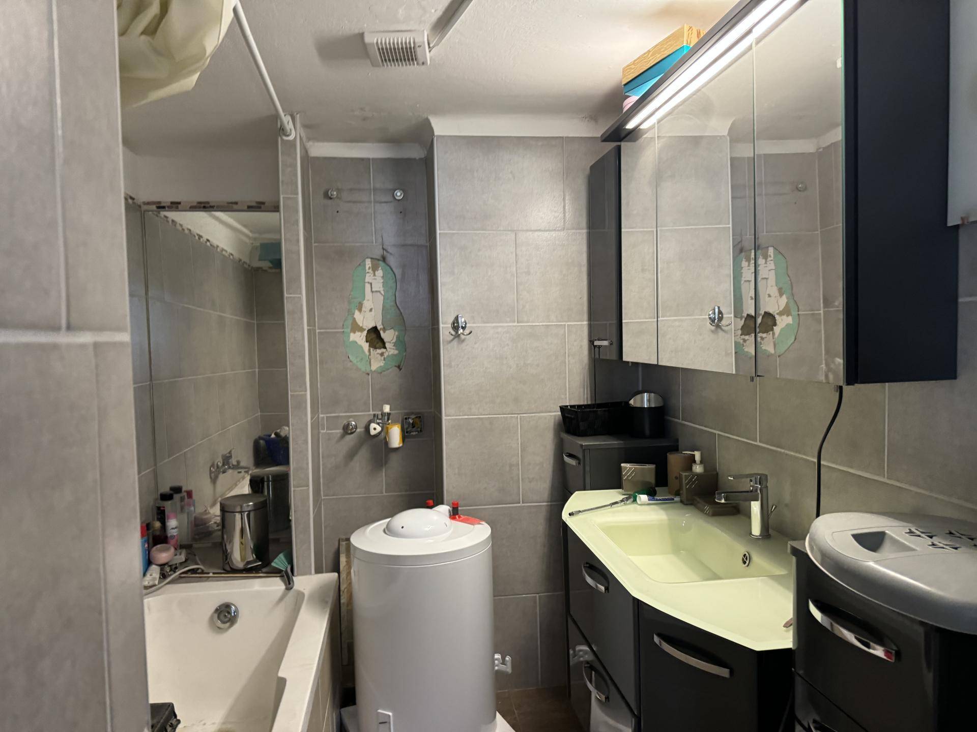 Badezimmer mit grauen Fliesen, Badewanne und einem Waschbecken mit Spiegelschrank.