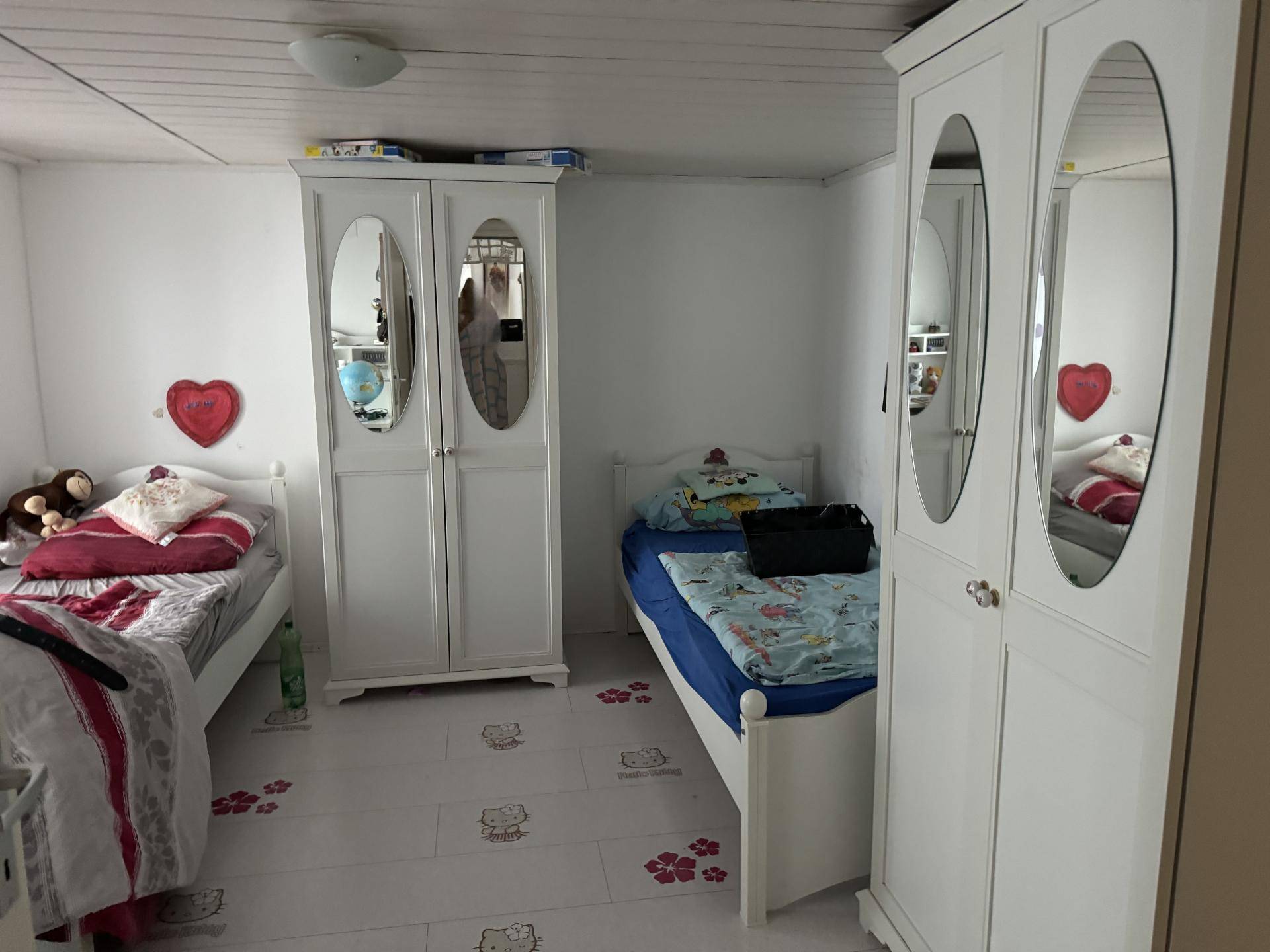 Kinderzimmer mit zwei Einzelbetten, weißen Schränken und einem verspielten Bodenmuster.