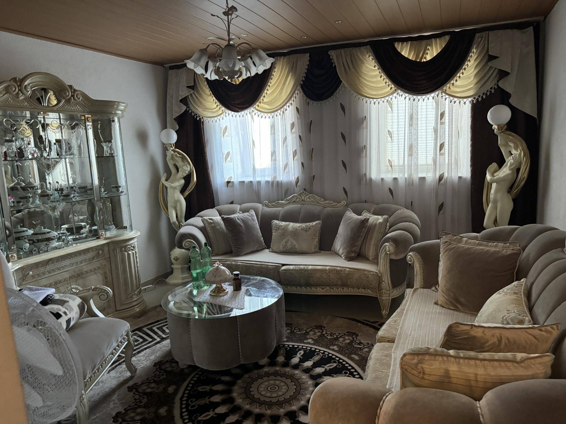 Elegantes Wohnzimmer im klassischen Stil mit plüschigen Sofas und einem verzierten Vitrinenschrank.