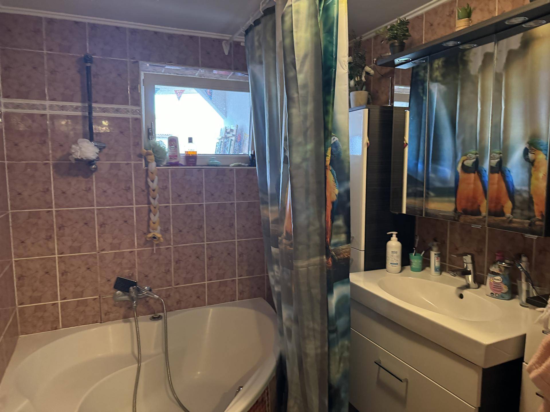 Badezimmer mit braunen Fliesen, Eckbadewanne und einem Waschbecken mit Spiegelschrank.