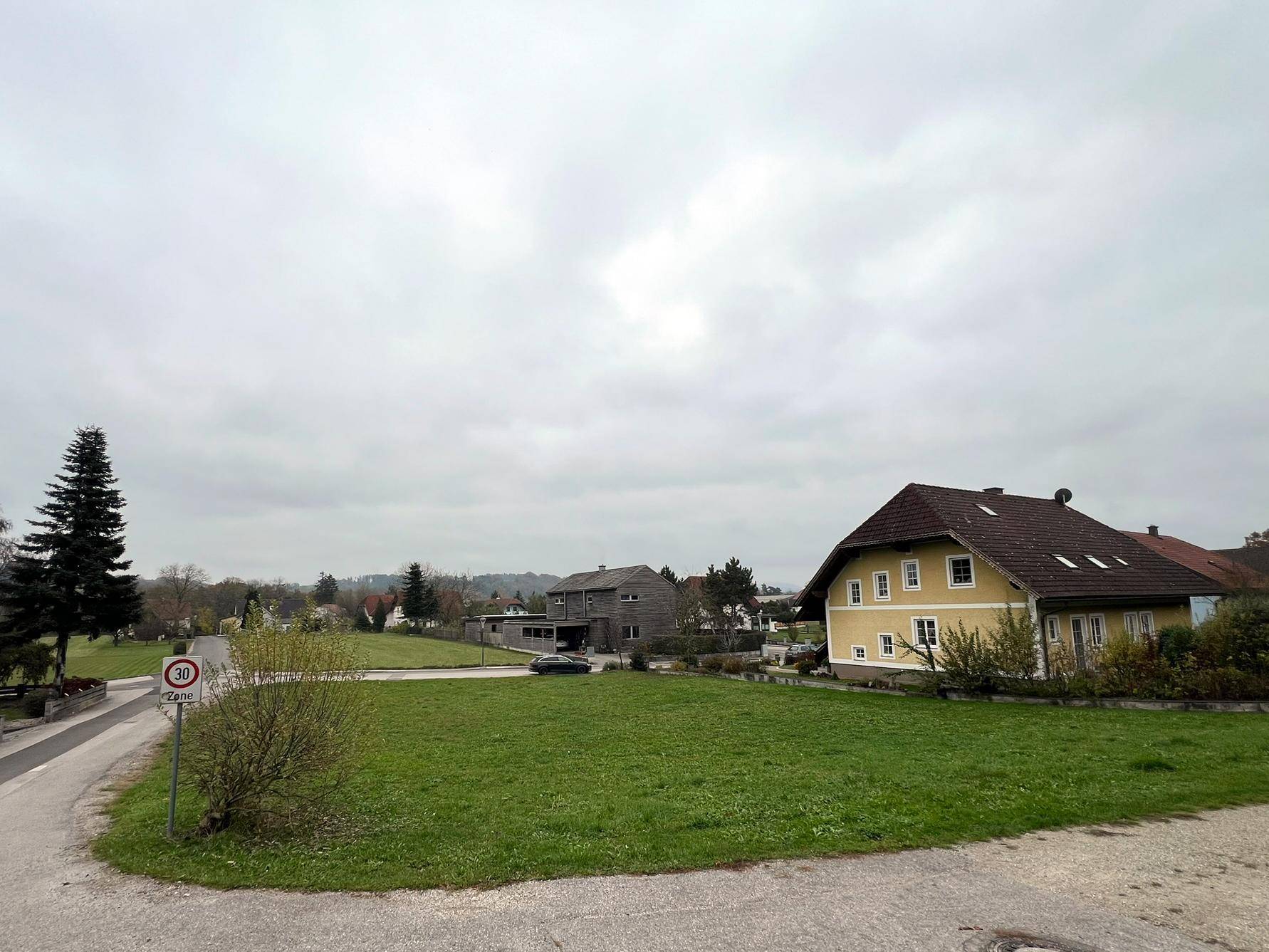 Weitläufiger Blick auf das Grundstück mit Rasenfläche, umgeben von weiteren Häusern und ländlicher Umgebung.