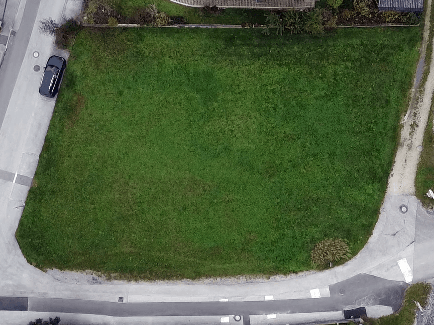 Senkrechte Luftaufnahme eines großen, rechteckigen Rasengrundstücks mit angrenzender Straße und parkendem Auto.