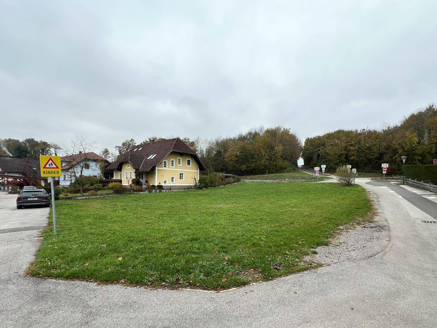 Weitläufiger Blick auf das grüne Grundstück mit angrenzender Straße und Häusern in ländlicher Umgebung.