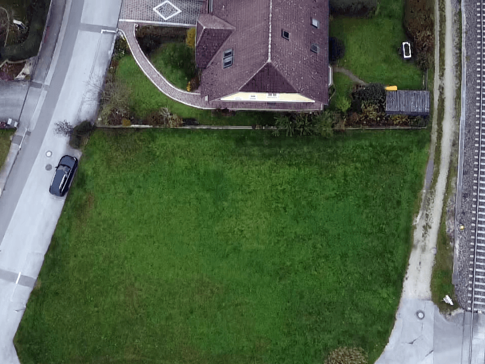 Luftaufnahme eines Hauses mit großem Rasengrundstück, angrenzender Straße und Bahnlinie im Herbst.