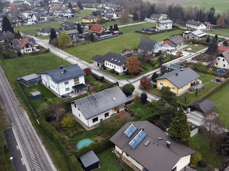 Luftaufnahme einer Wohnsiedlung mit verschiedenen Häusern, Gärten und einigen Dächern mit Solaranlagen.