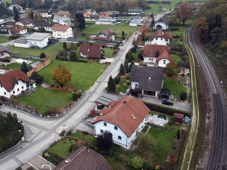 Luftaufnahme einer Wohnsiedlung mit Einfamilienhäusern, Gärten und einer parallel verlaufenden Bahnlinie.