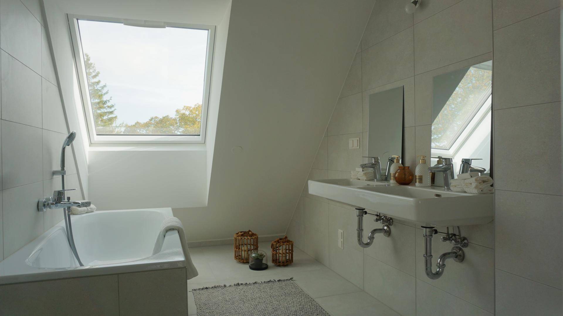 Modernes Badezimmer mit Badewanne, Doppelwaschbecken und einem Dachfenster für natürliches Licht.