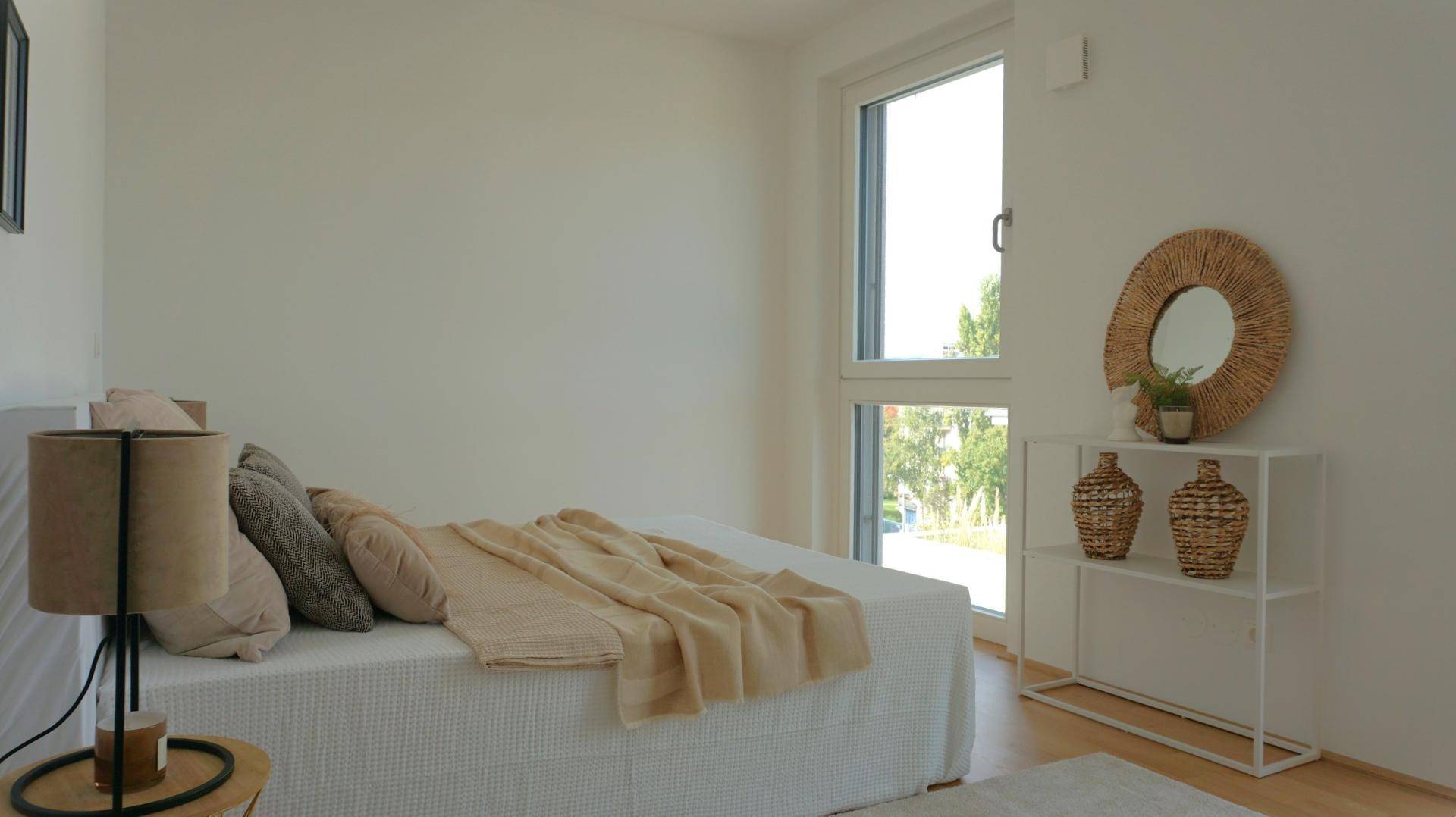 Schlafzimmer mit großem Fenster, Holzboden und minimalistischer Dekoration, die viel Licht hereinlässt.