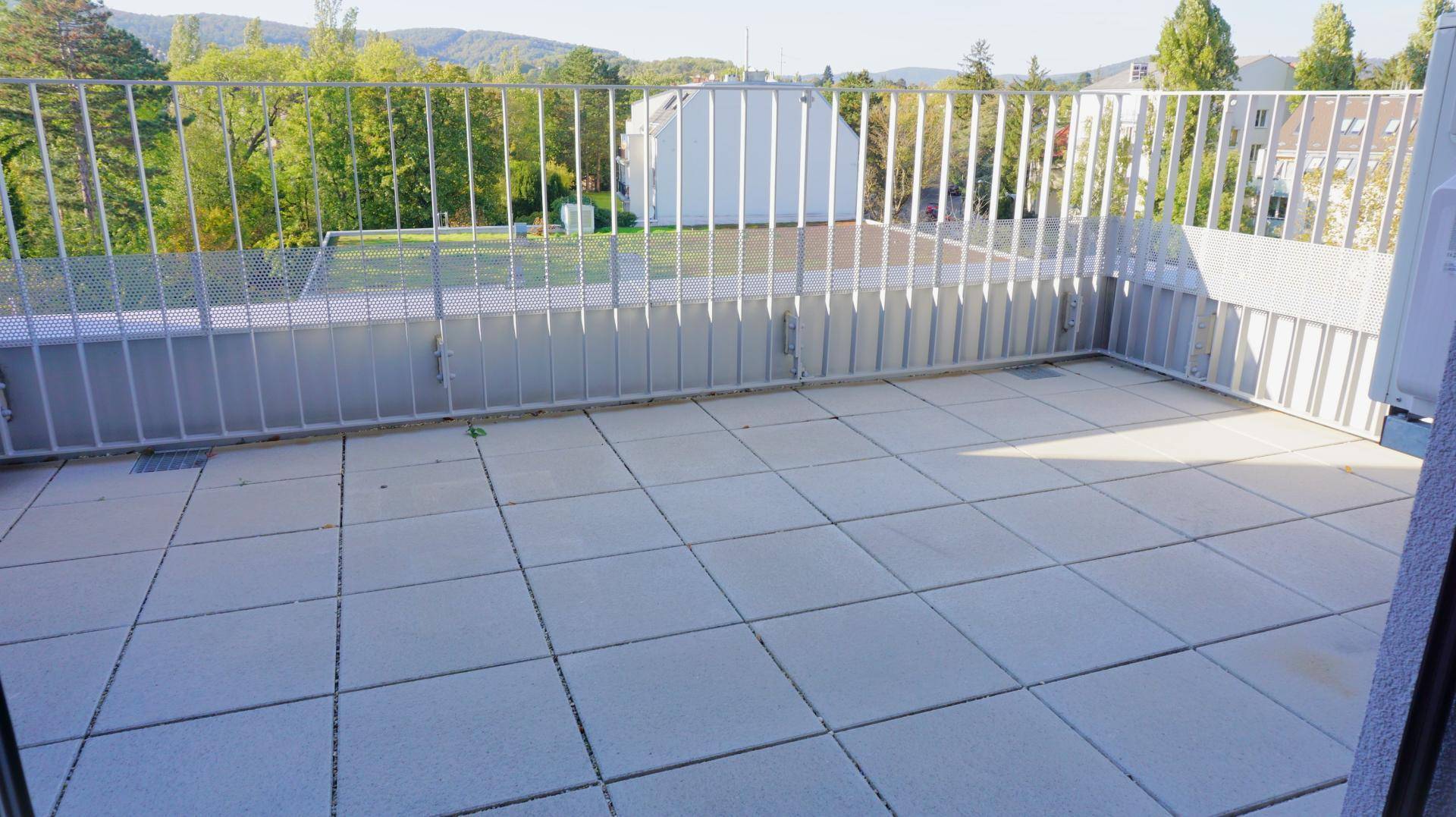 Große Dachterrasse mit Fliesenboden und einem weiten Blick auf die grüne Umgebung.