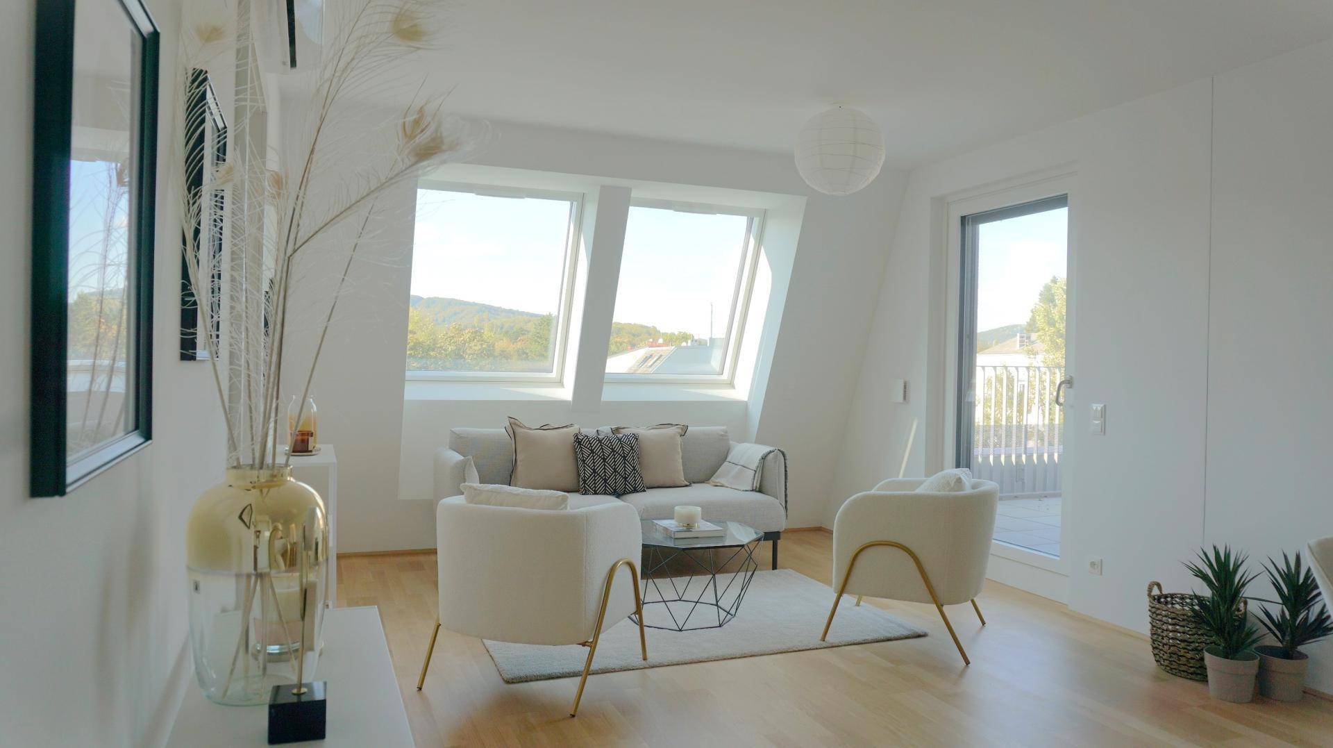 Gemütliches Wohnzimmer mit großen Dachfenstern, hellen Möbeln und einem weiten Blick ins Grüne.