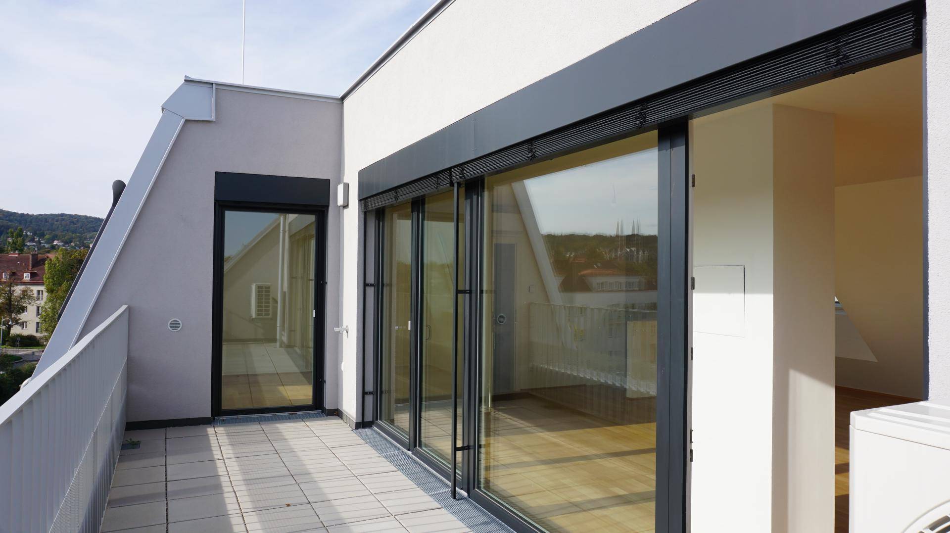 Balkon mit großen Glasschiebetüren und Blick auf die Umgebung, ausgestattet mit Rollläden.