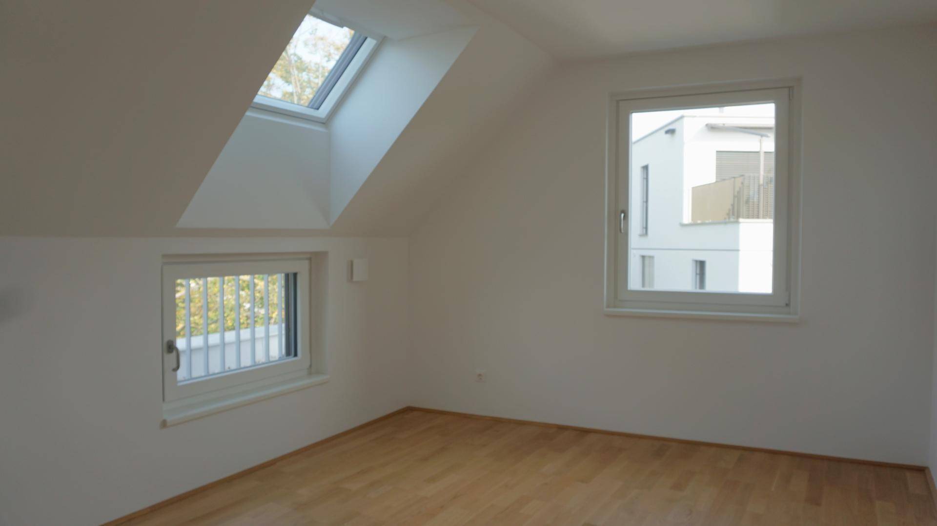 Heller Raum im Dachgeschoss mit Holzboden, einem Dachfenster und einem weiteren Fenster.