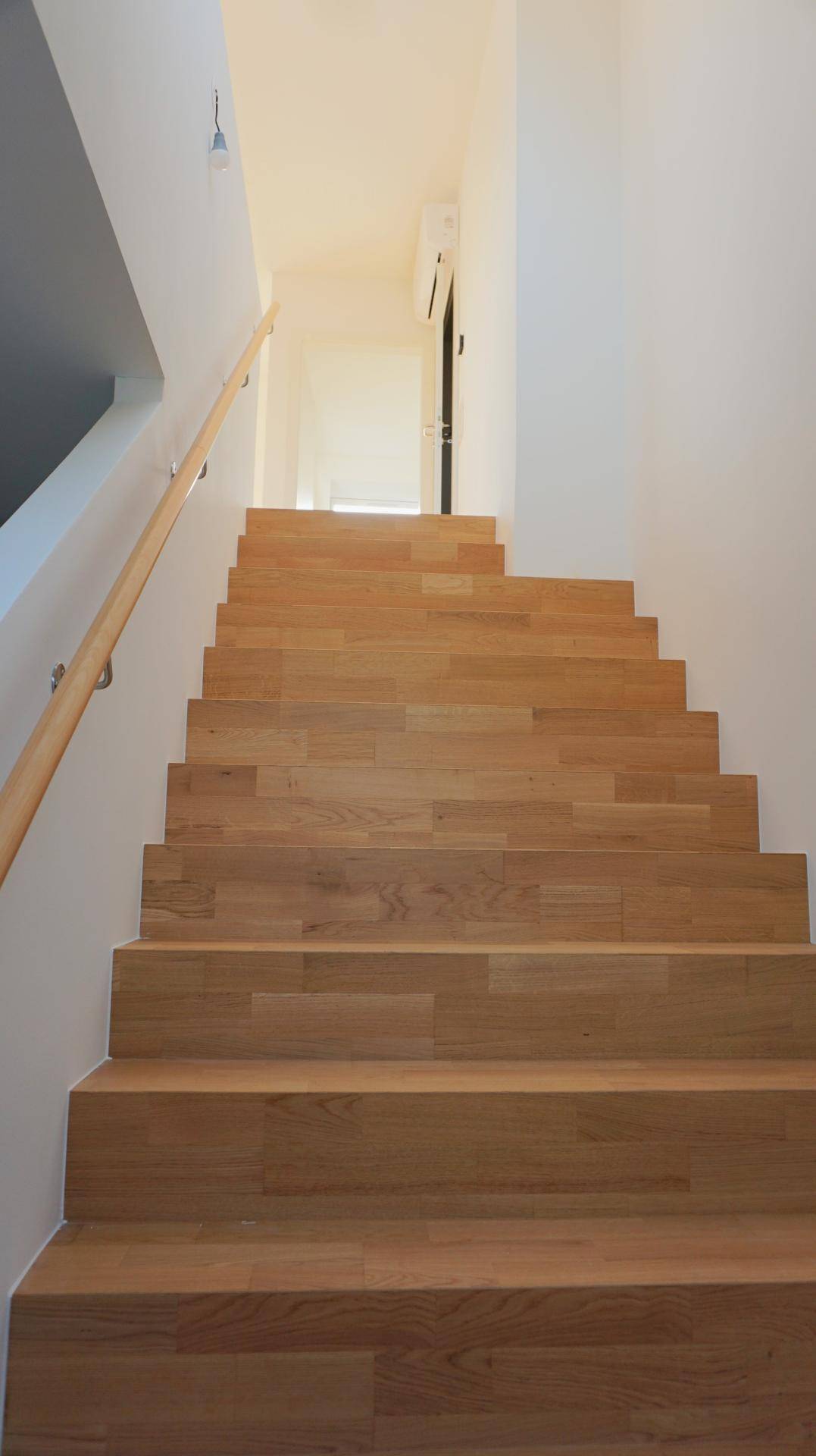 Helle Holztreppe mit Handlauf, die verschiedene Ebenen des Hauses miteinander verbindet.
