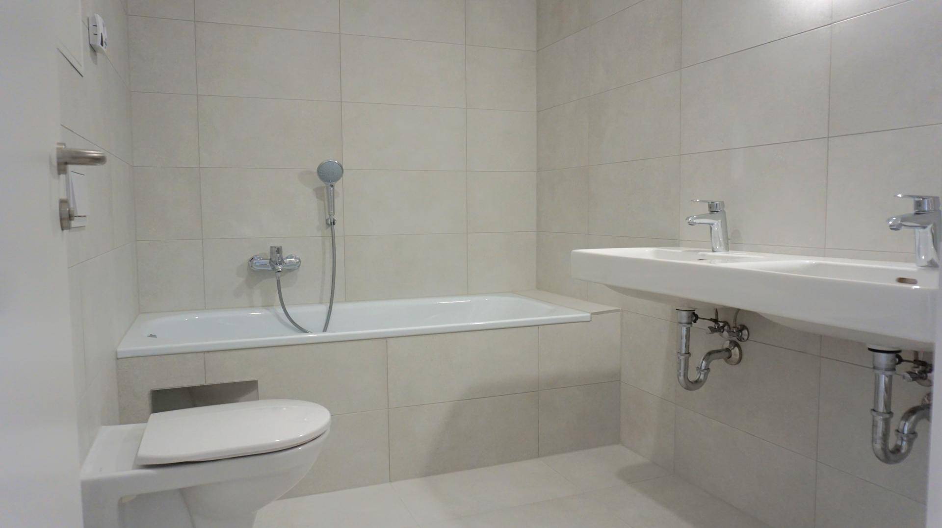 Modernes Badezimmer mit hellen Fliesen, Badewanne, wandhängendem WC und Doppelwaschbecken.
