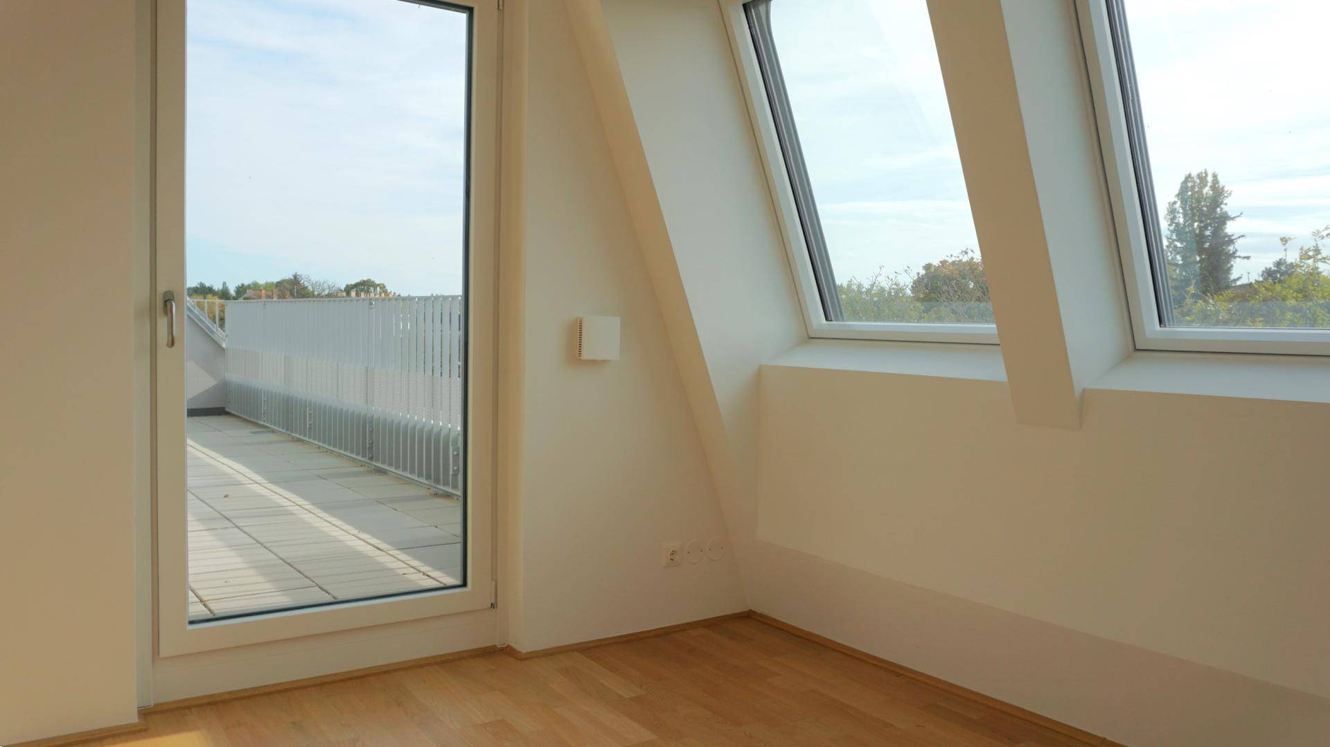 Leerer Raum im Dachgeschoss mit Holzboden, Dachfenstern und Zugang zu einem Außenbereich.