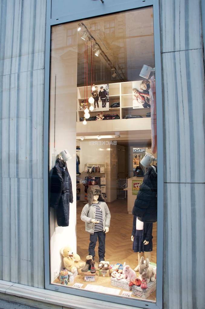 Schaufenster eines Ladens mit Kindermode und Dekoration, reflektiert die Umgebung.