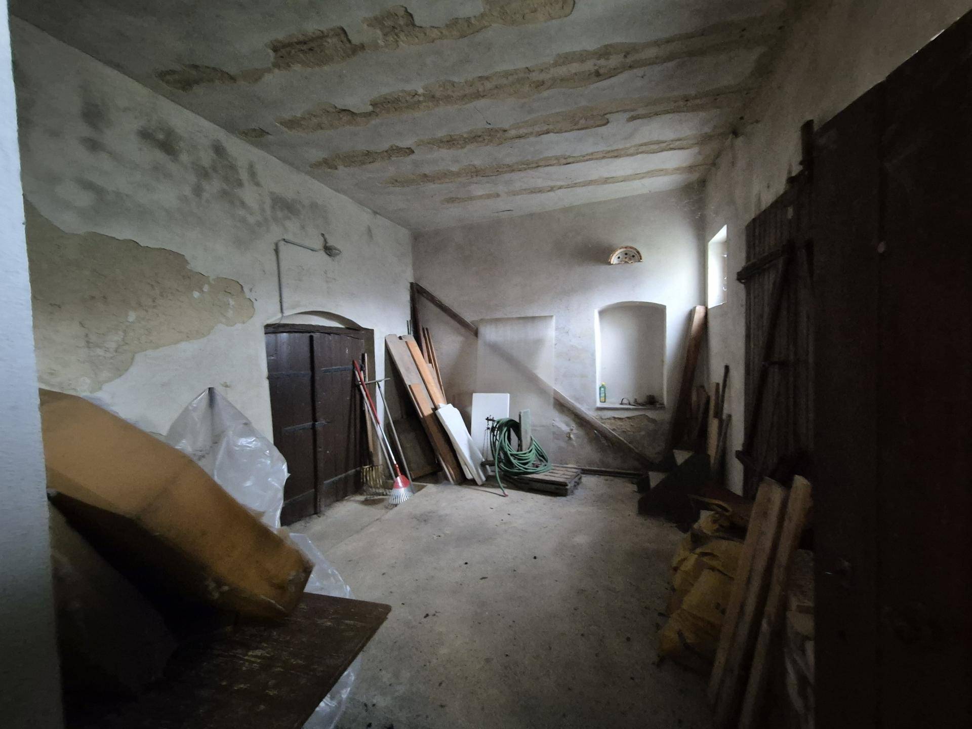 Großer, ungenutzter Raum mit sichtbaren Deckenbalken, rauen Wänden und Betonboden.