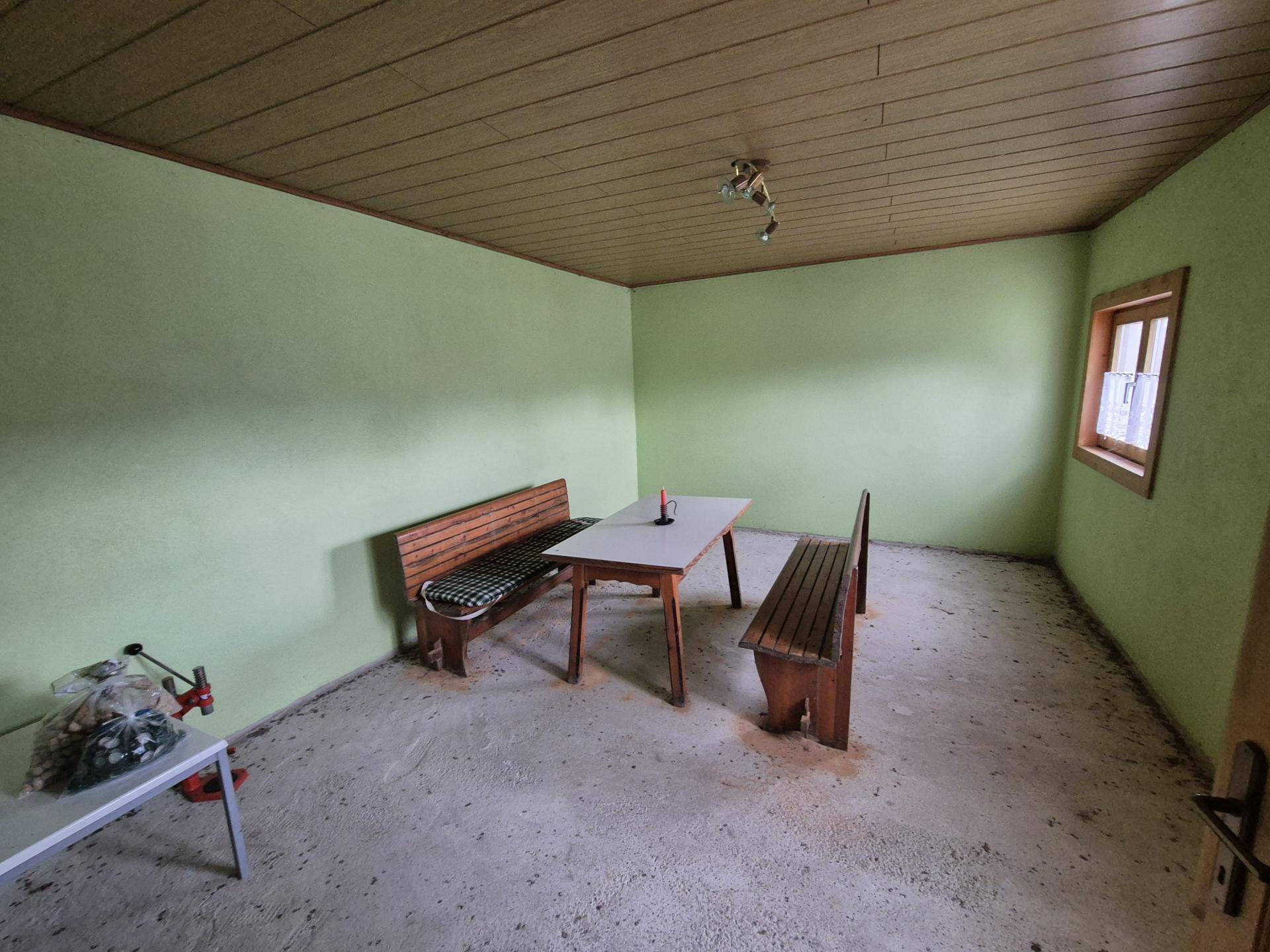 Einfacher Raum mit Holzbänken, einem Tisch, grünen Wänden und Holzdeckenverkleidung.
