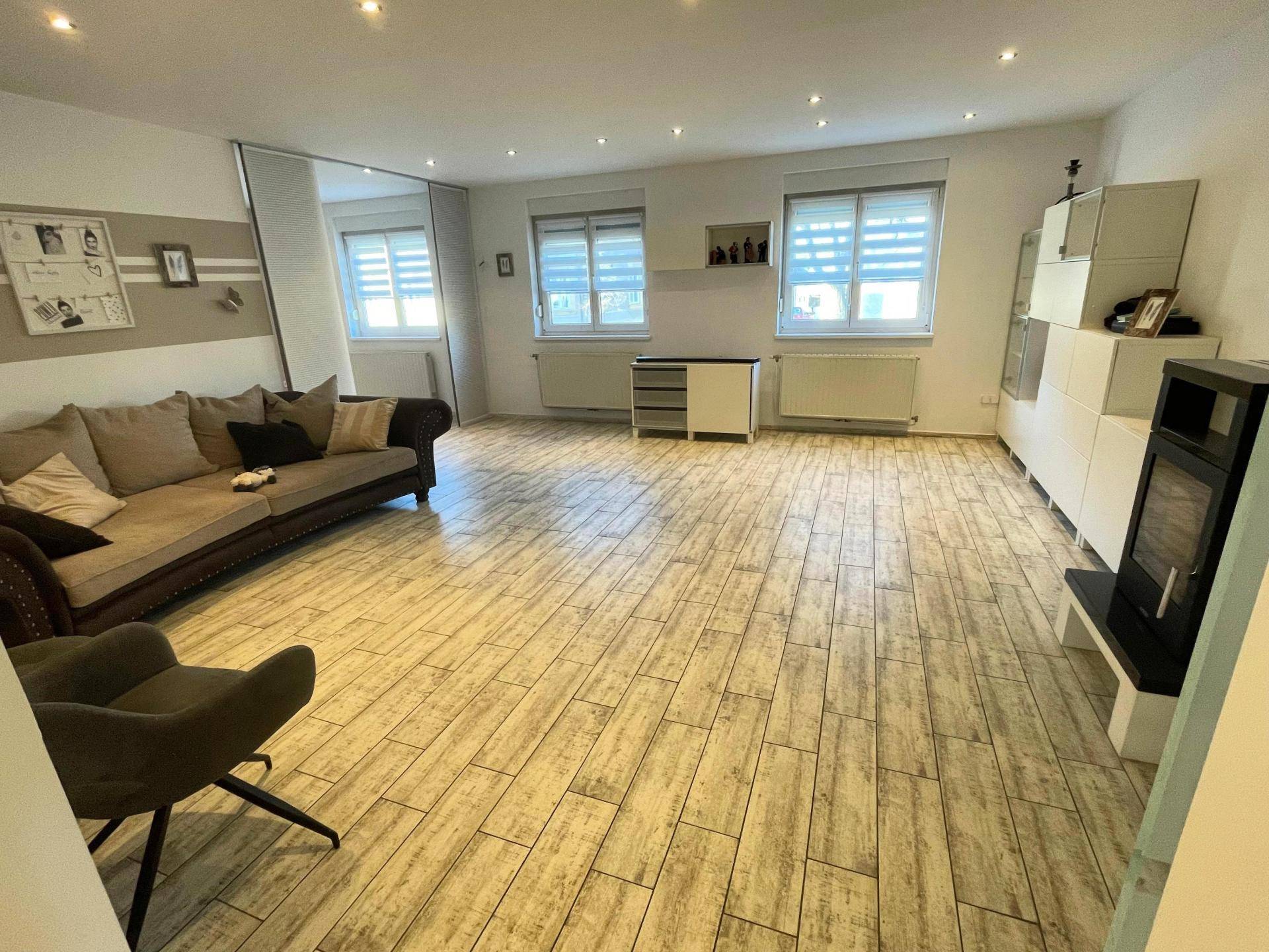 Geräumiges Wohnzimmer mit hellem Fliesenboden in Holzoptik, bequemer Couch und natürlichem Lichteinfall.