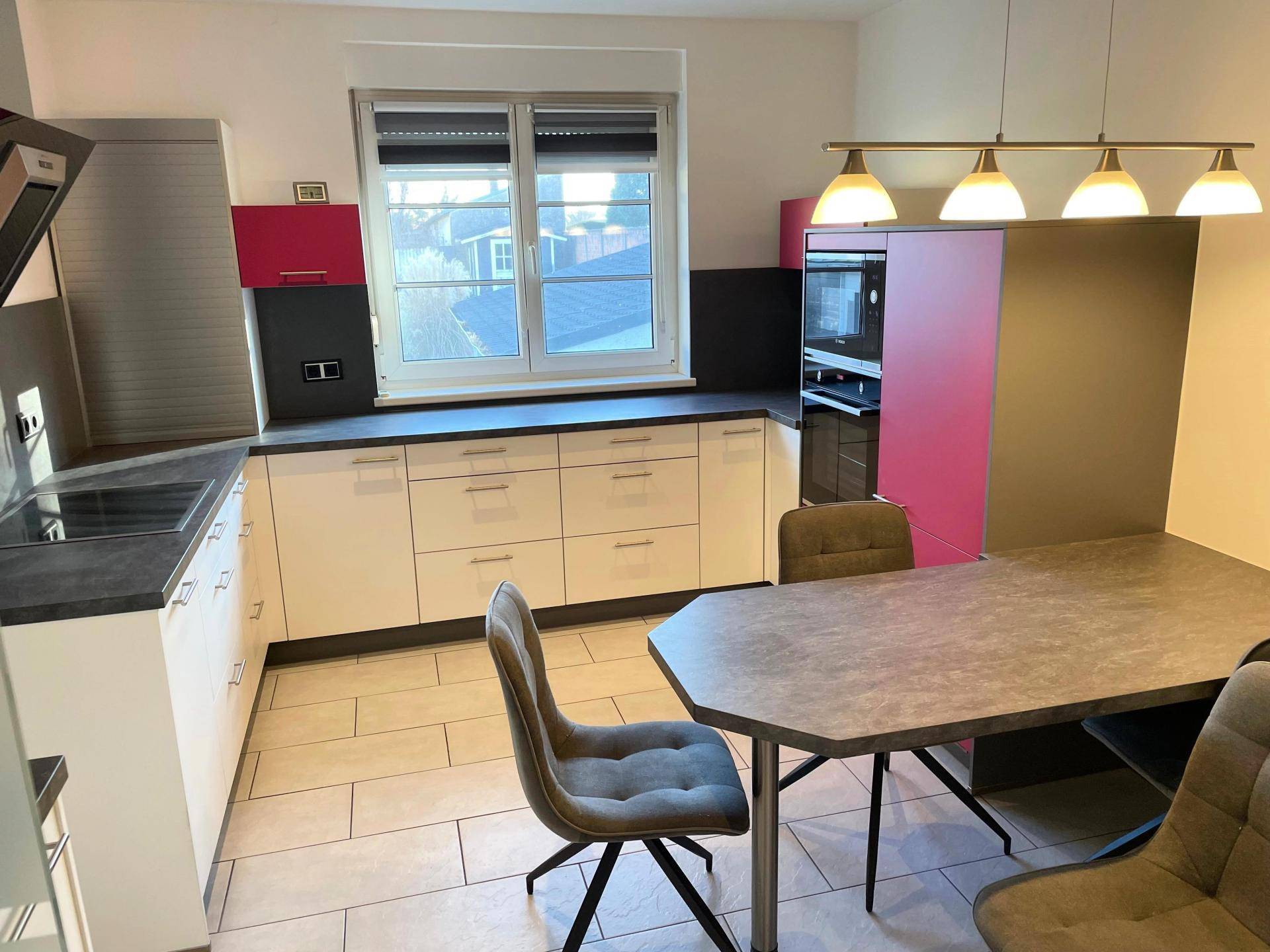 Moderne Küche mit weißen und pinken Schränken, Essbereich und Fenster mit Blick nach draußen.