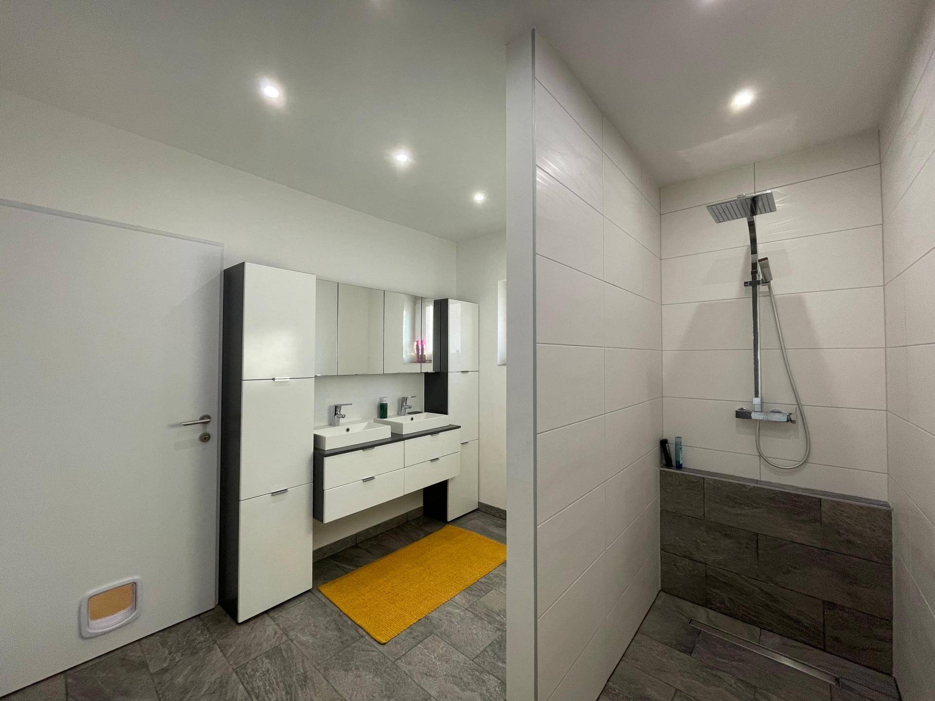Modernes Badezimmer mit Doppelwaschbecken, großer begehbarer Dusche und eleganten Fliesen.