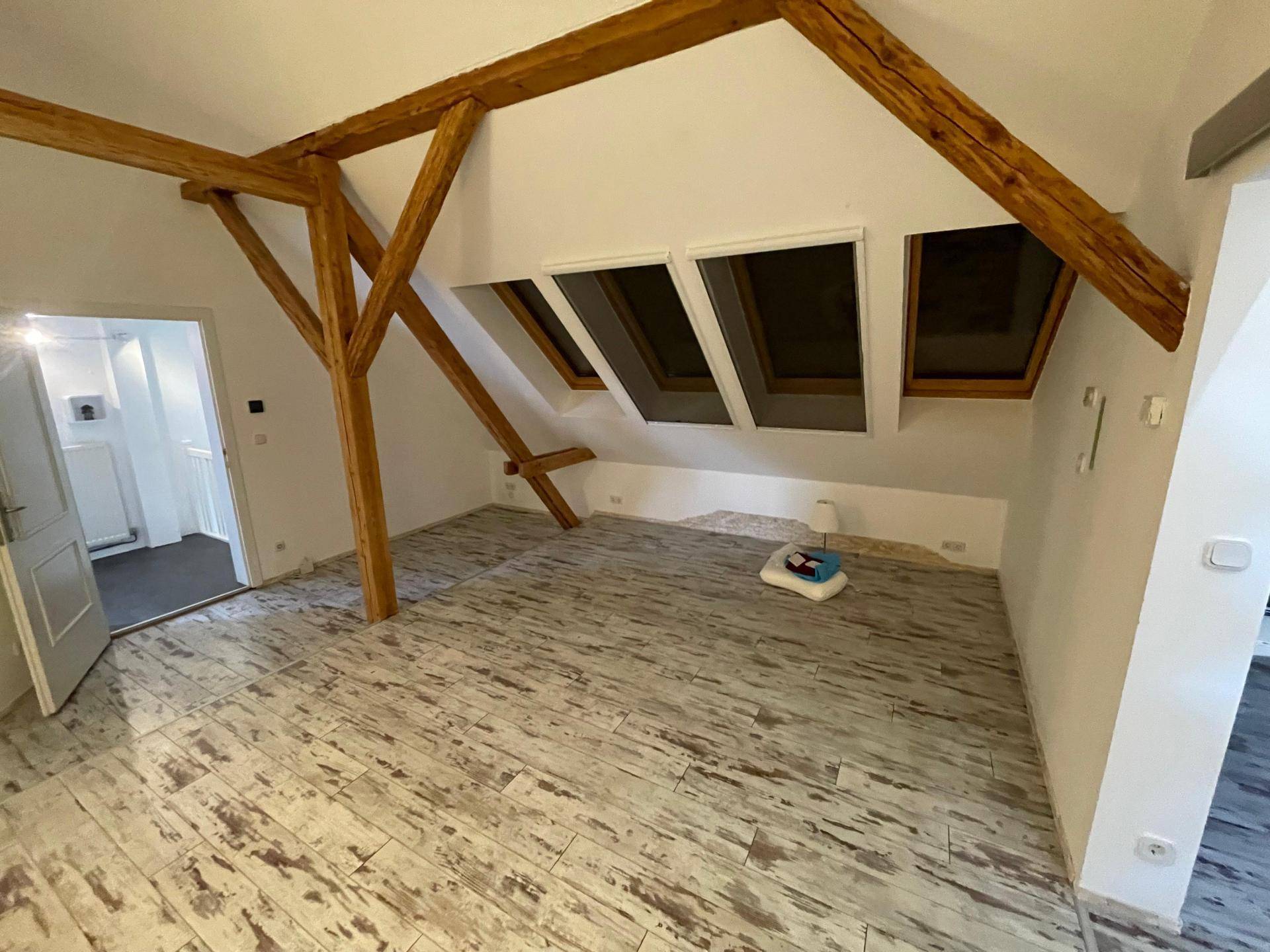 Ausgebauter Dachboden mit sichtbaren Holzbalken, Dachfenstern und hellem Fliesenboden in Holzoptik.