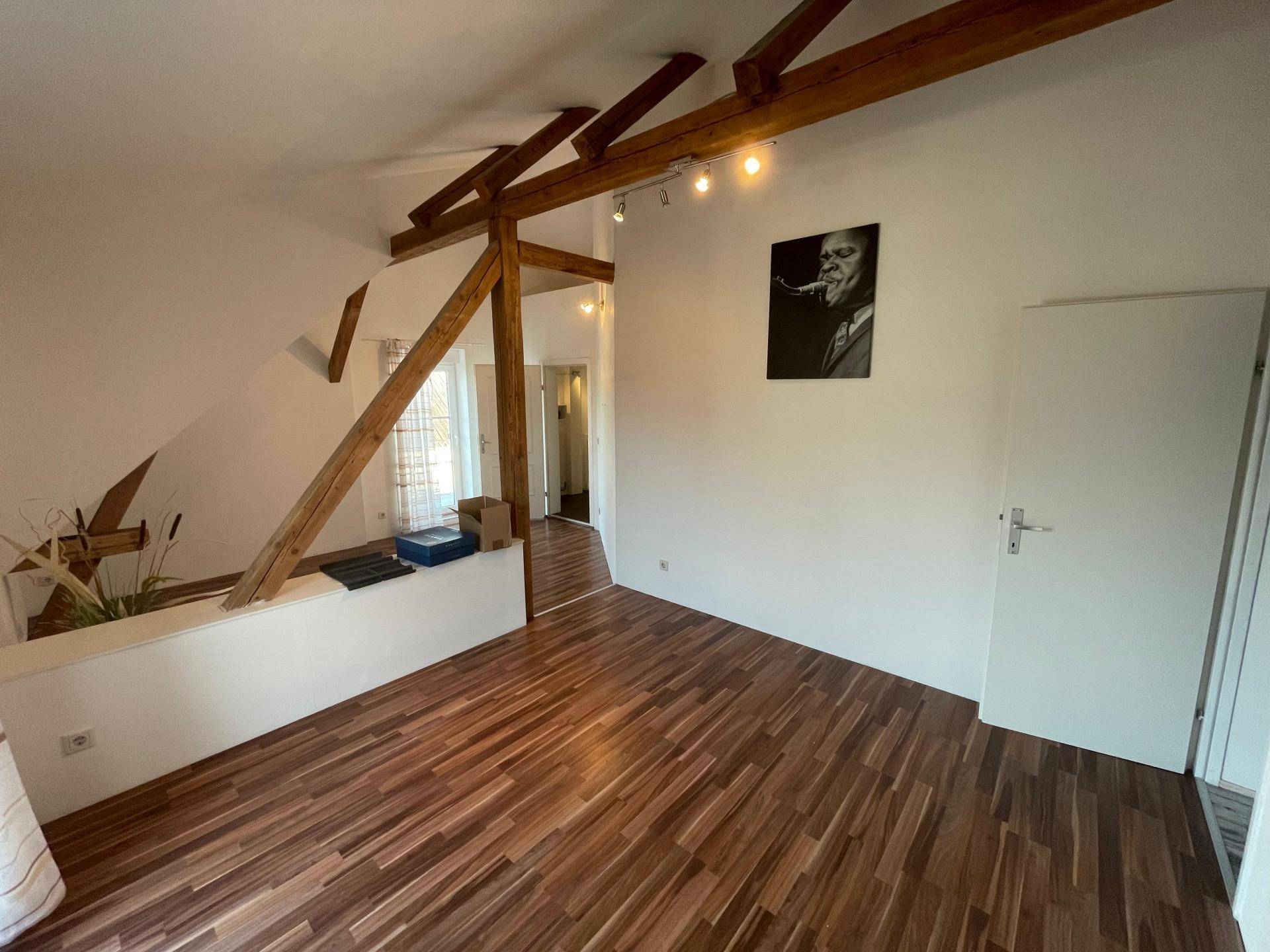 Helles Dachzimmer mit Holzbalken, Holzboden und Blick auf den angrenzenden Flur.