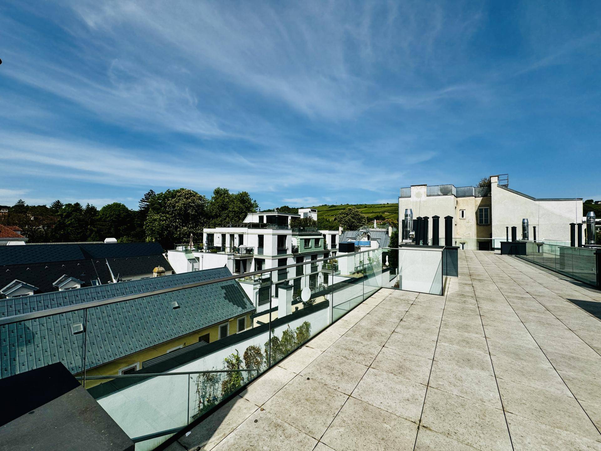 Weitläufige Dachterrasse mit moderner Architektur und Blick auf umliegende Gebäude unter blauem Himmel.