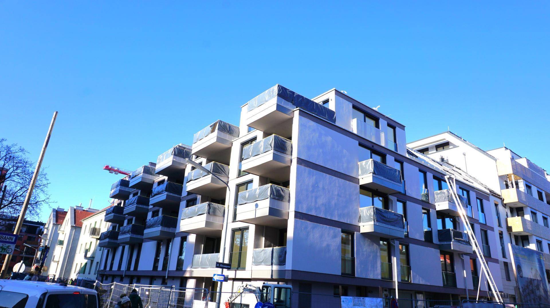 Modernes Neubaugebäude mit vielen Balkonen und großen Fenstern unter klarem blauem Himmel.