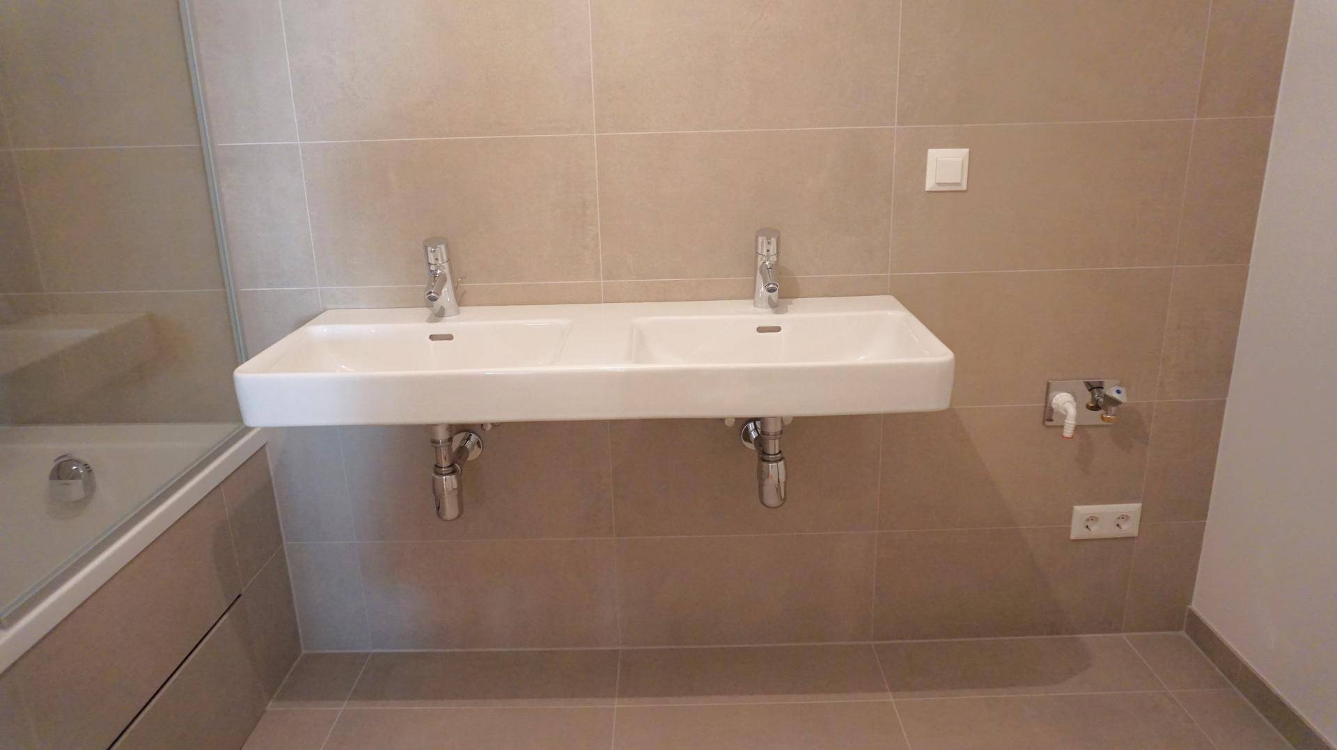 Modernes Badezimmer mit Doppelwaschbecken und beigefarbenen Fliesen, neuwertig und hell.