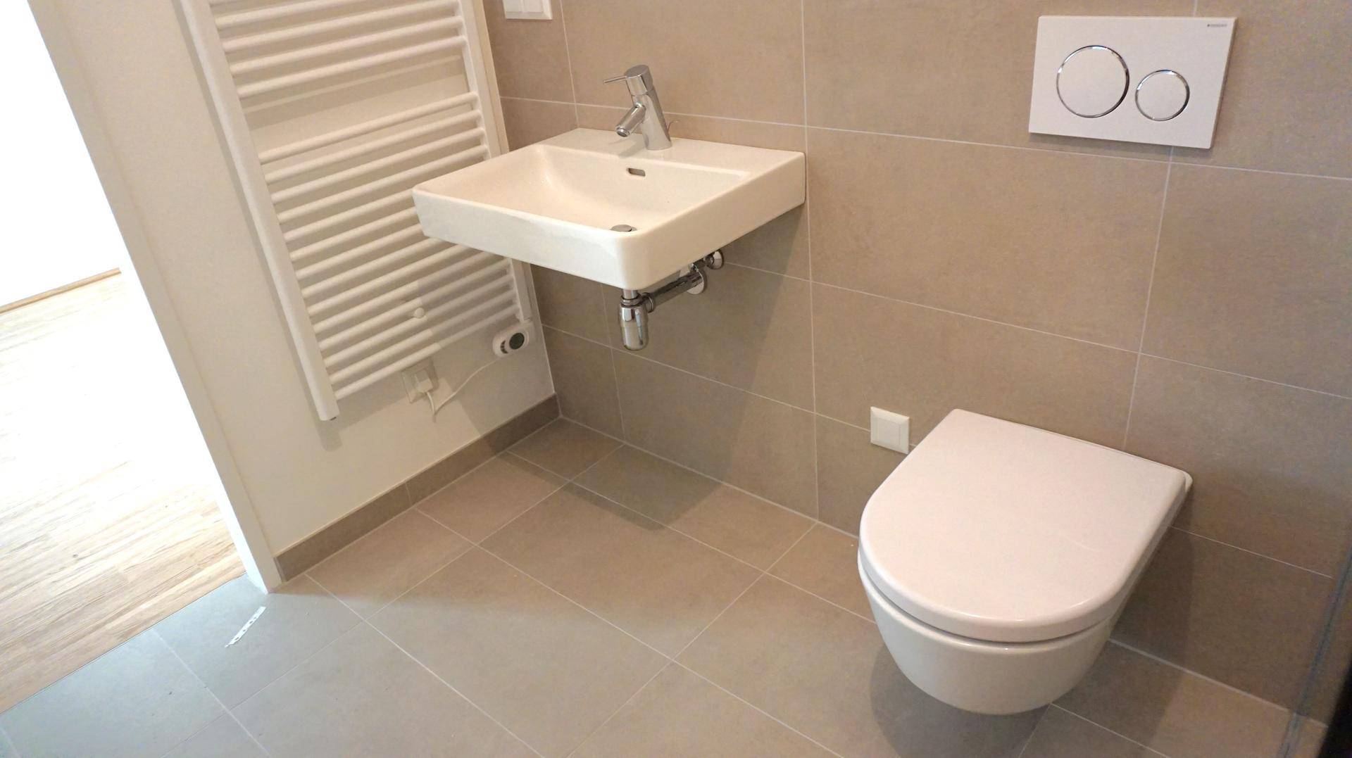 Modernes Gäste-WC mit Heizkörper, wandhängender Toilette und kleinem Waschbecken, hell gefliest.