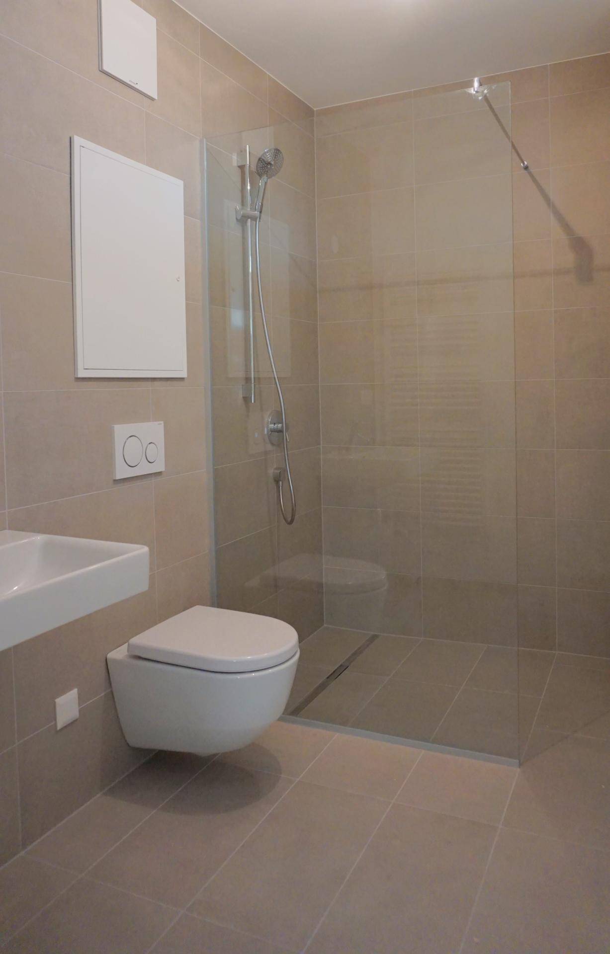 Modernes Badezimmer mit ebenerdiger Dusche, wandhängender Toilette und beigefarbenen Fliesen.