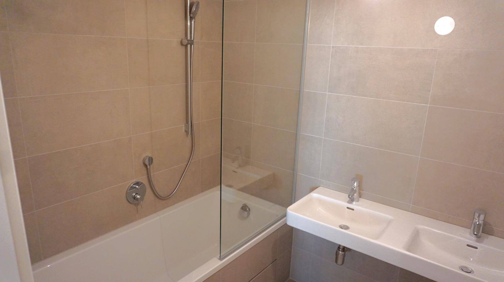 Modernes Badezimmer mit Badewanne, Duschabtrennung und Doppelwaschbecken in neutralen Farben.